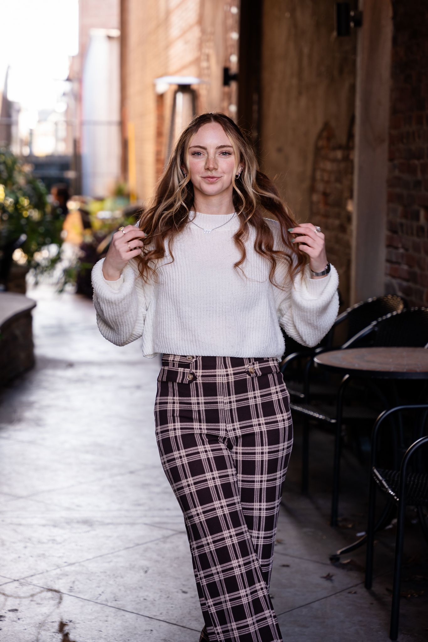 Casual street style look with white sweater and plaid pants photographed under city archway.