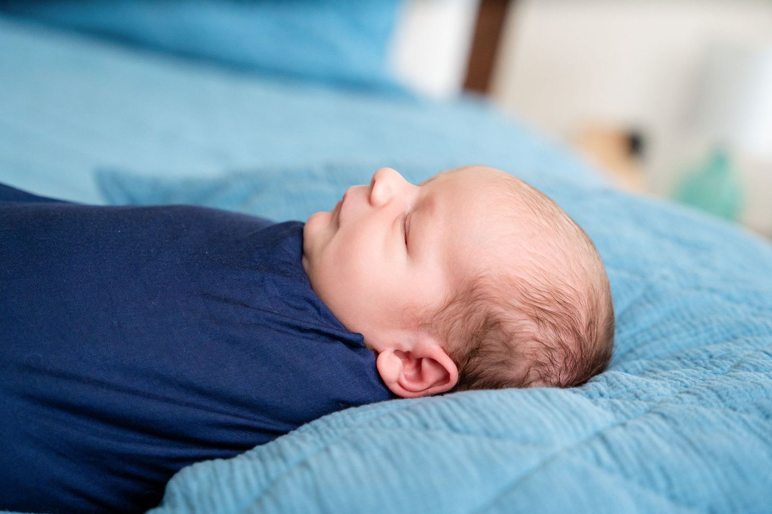 Newborn baby sleeping peacefully on blue quilted bedding.