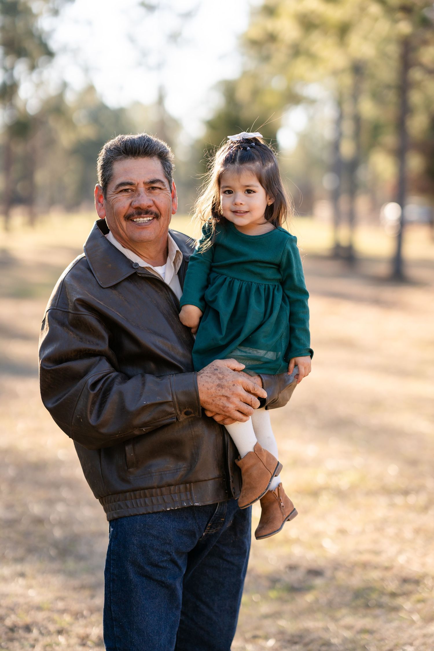 A sweet moment between family members is captured in warm sunlight against a natural outdoor backdrop.