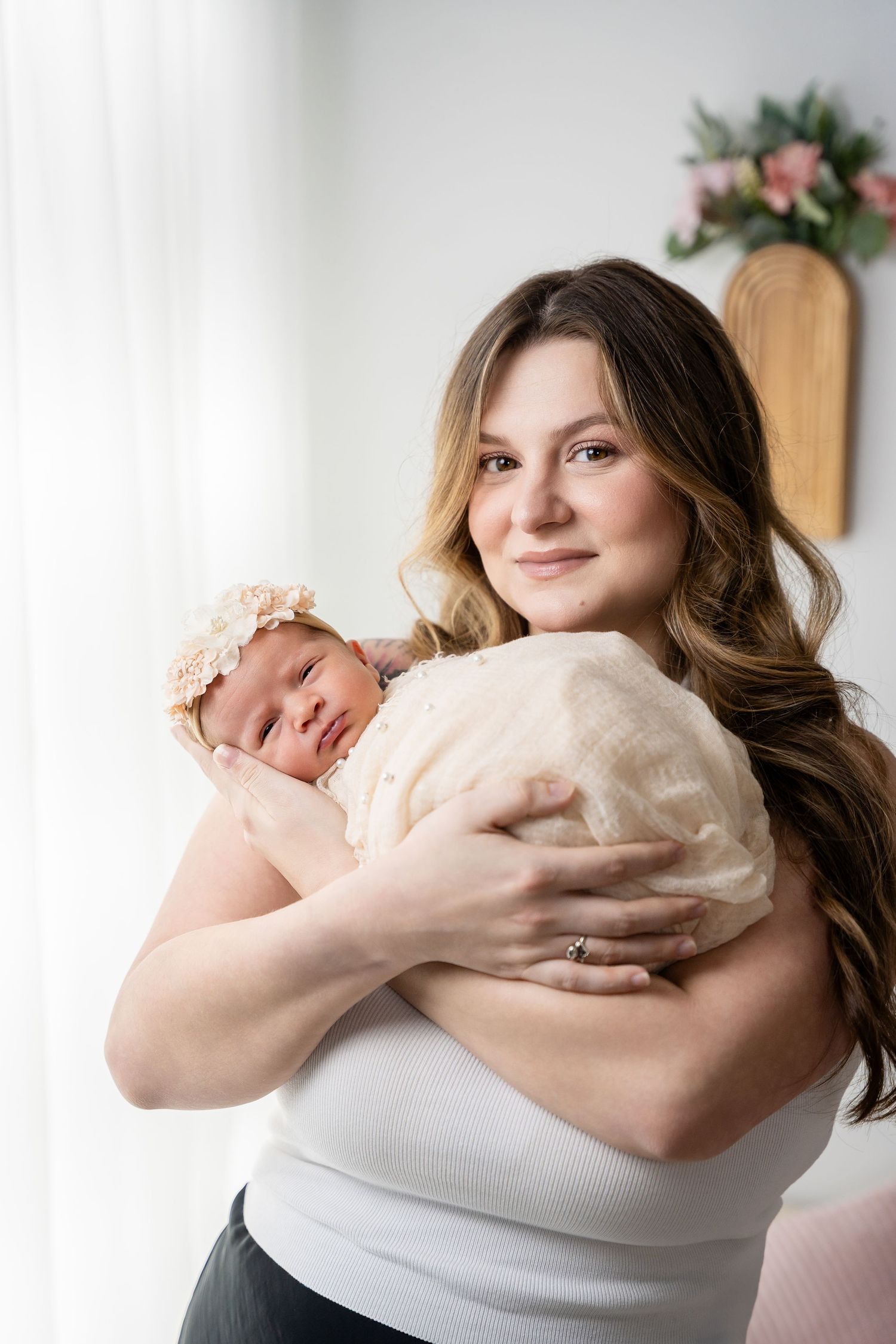 Tender moment captured in soft lighting as a newborn is held close in a cream-colored outfit.