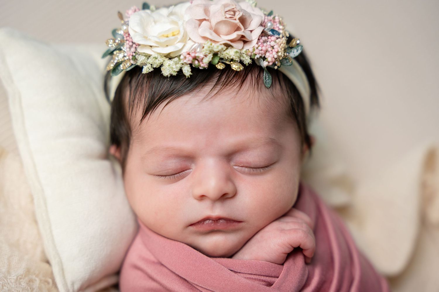 Sleeping newborn wrapped in pink swaddle wearing delicate floral crown with roses and baby's breath.