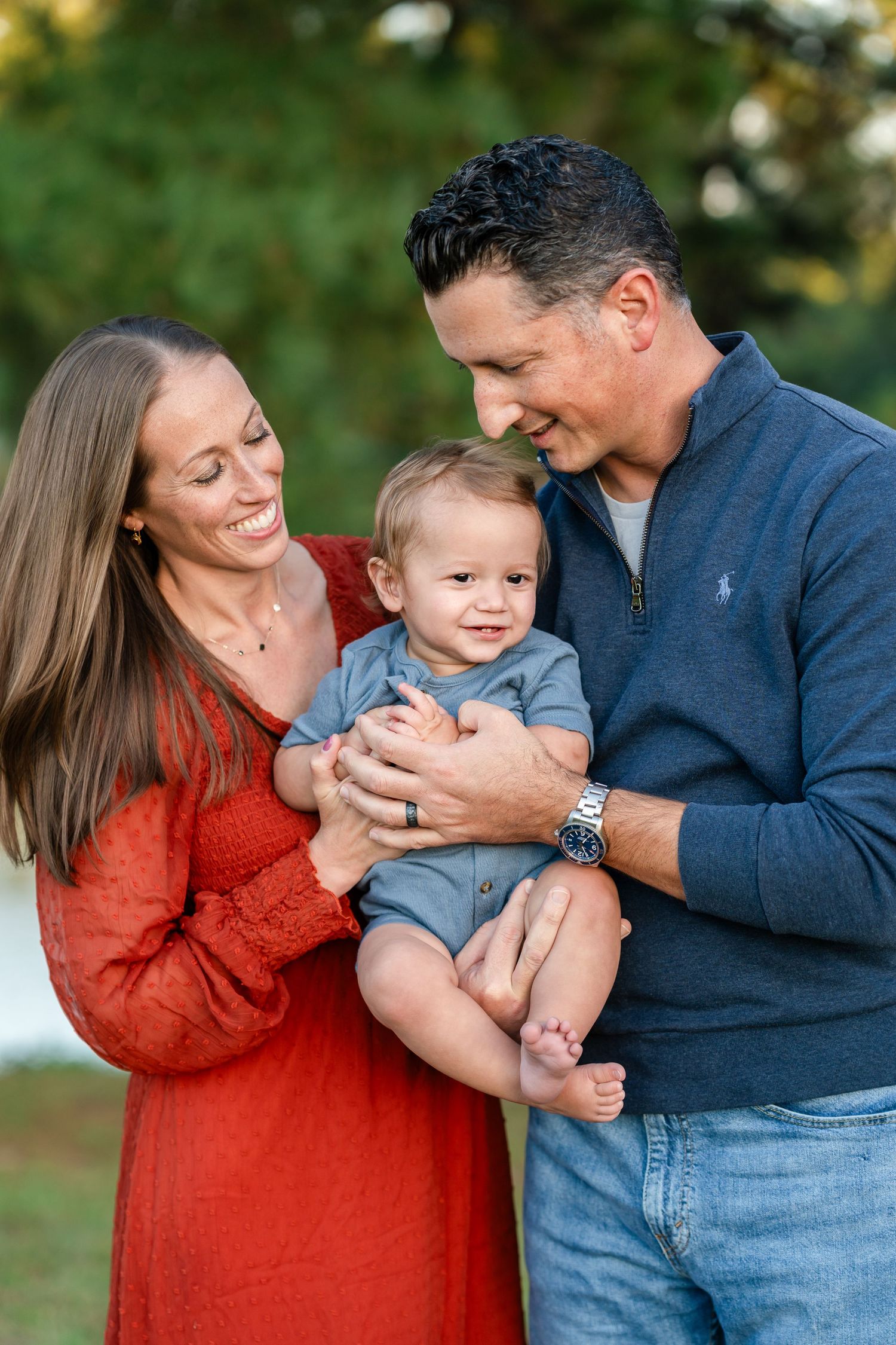 A family shares joyful moments together outdoors, wearing red and blue clothing while playing and laughing.