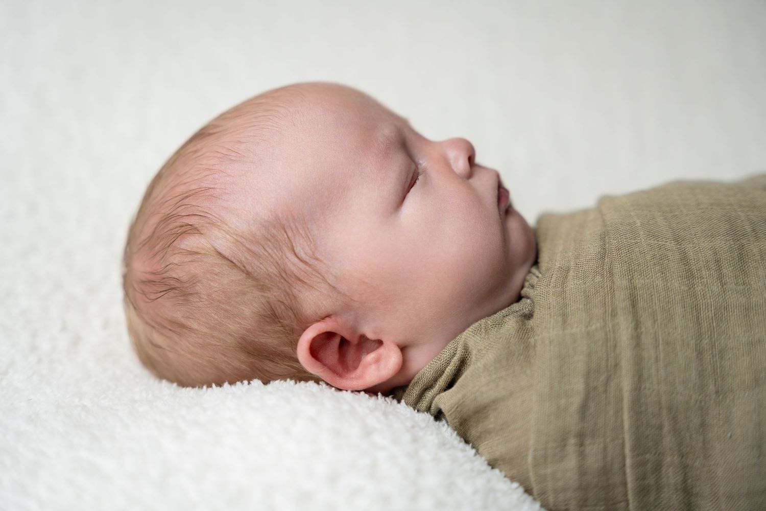 Side profile shots of peaceful sleeping newborn wrapped in tan fabric.