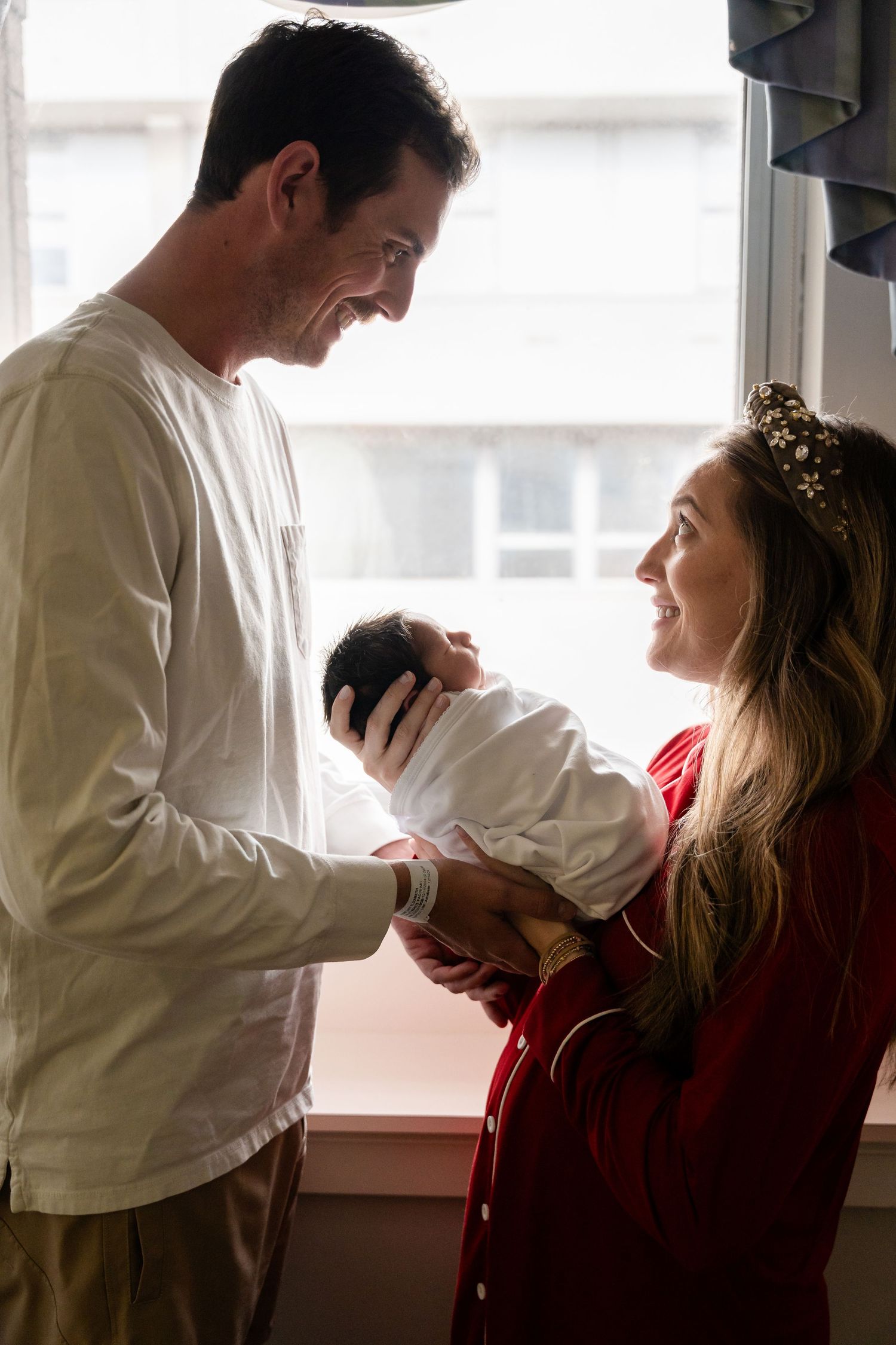 Tender family moment by large window with natural light.
