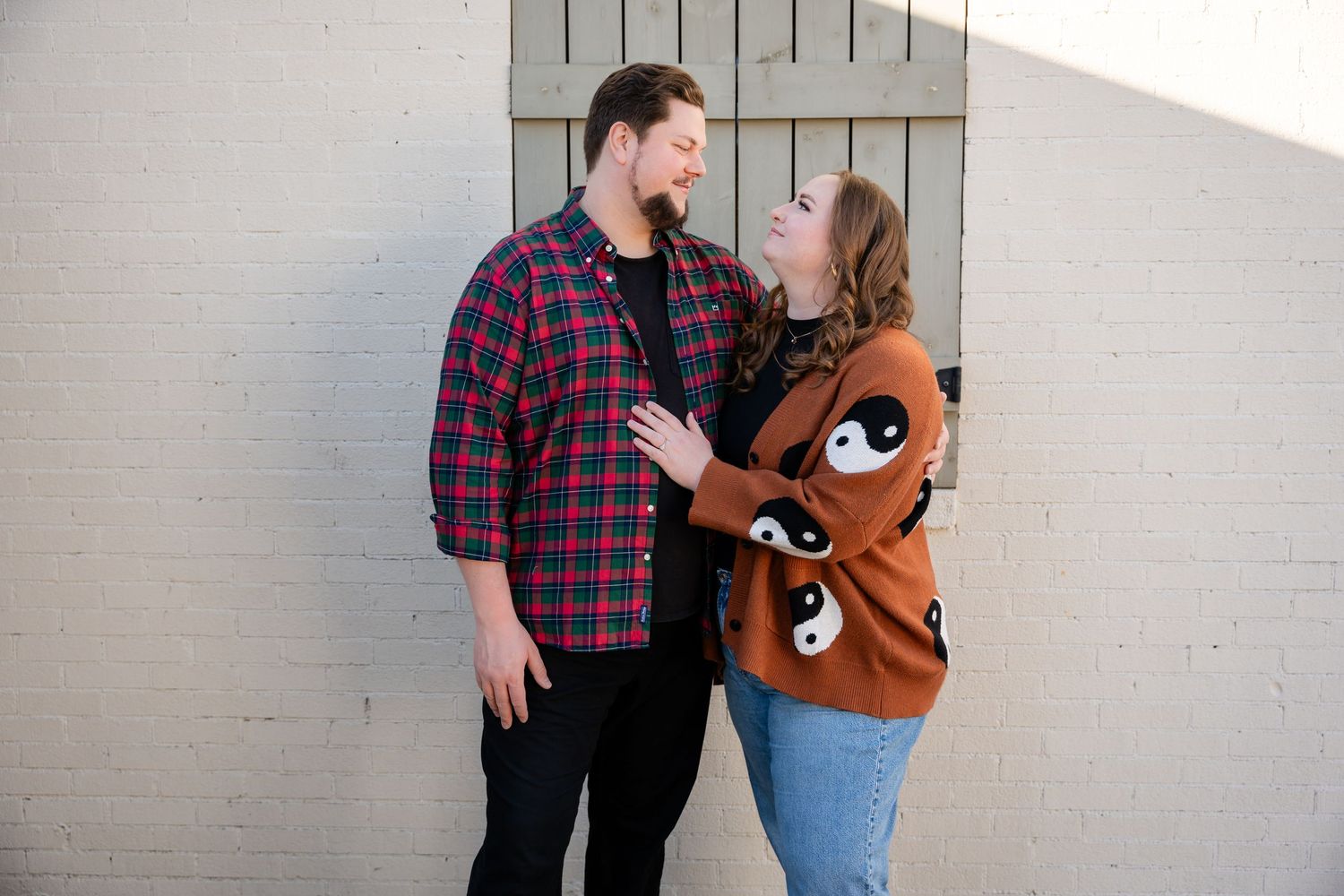 Couple embracing against white wall during engagement photoshoot.