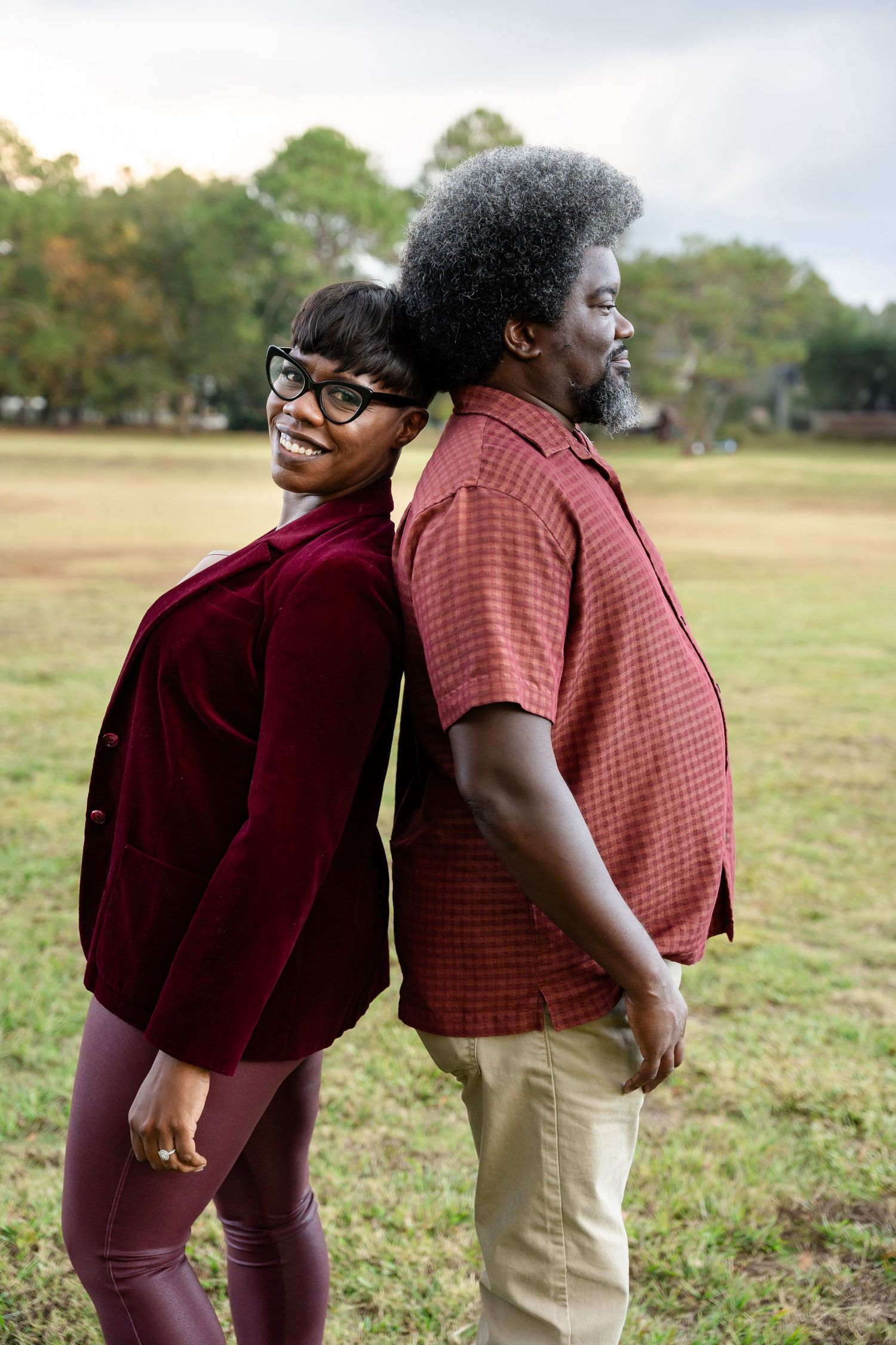 Two people standing back-to-back outdoors in casual attire against natural landscape.