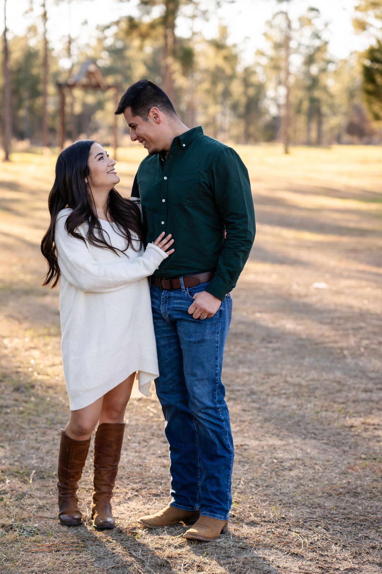 A couple in contrasting outfits shares an intimate moment in a sunlit forest clearing.