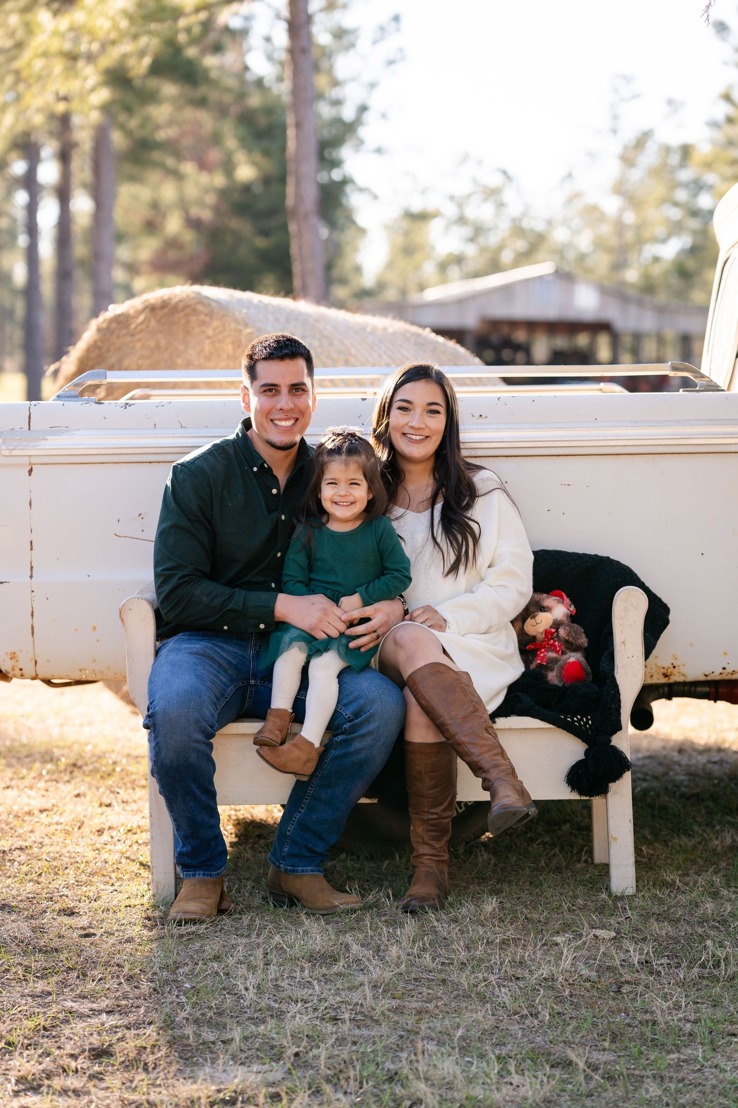 A family sits together on a white bench during their outdoor portrait session.