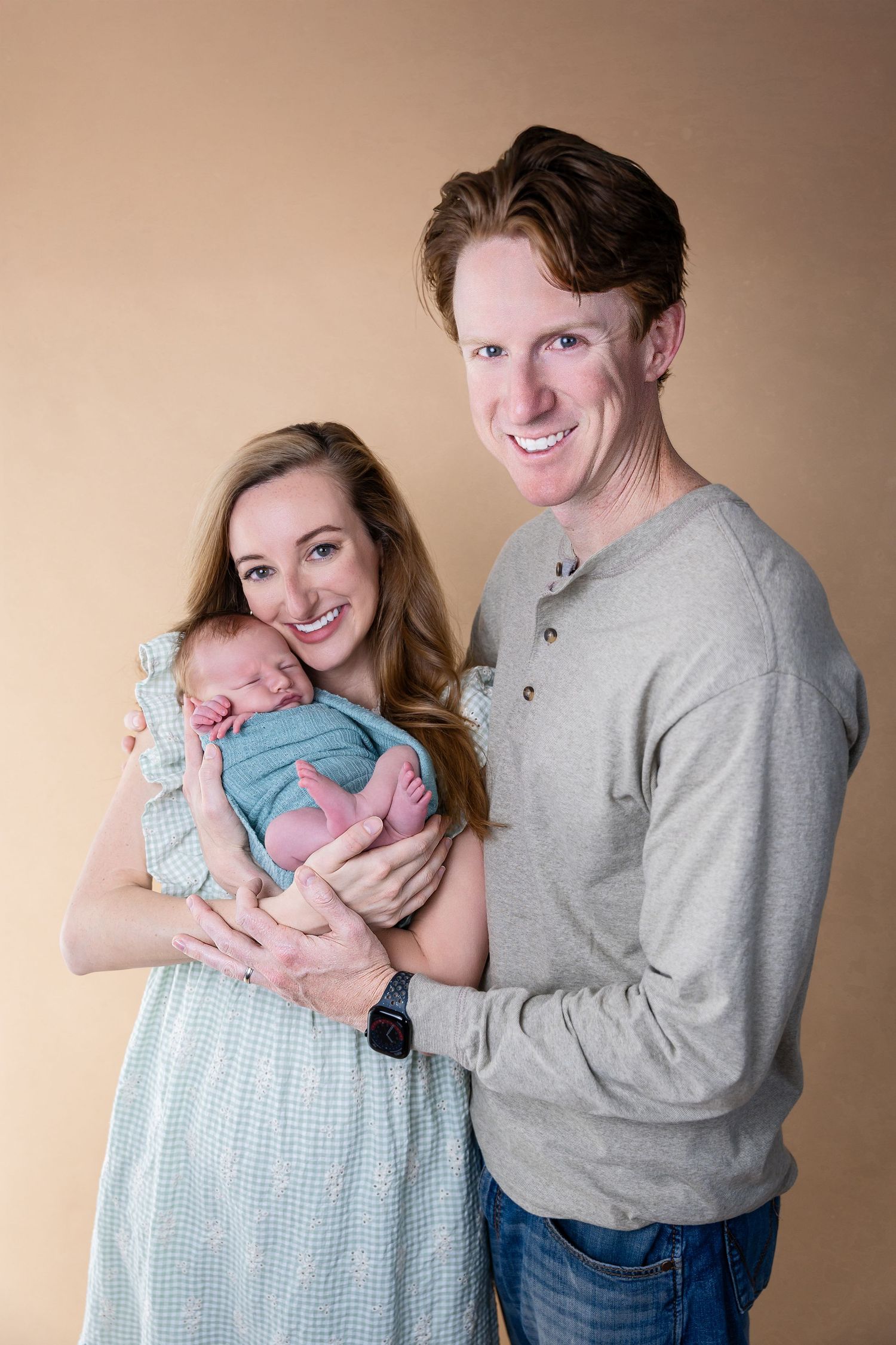 Happy couple in casual attire holding their newborn in blue outfit.