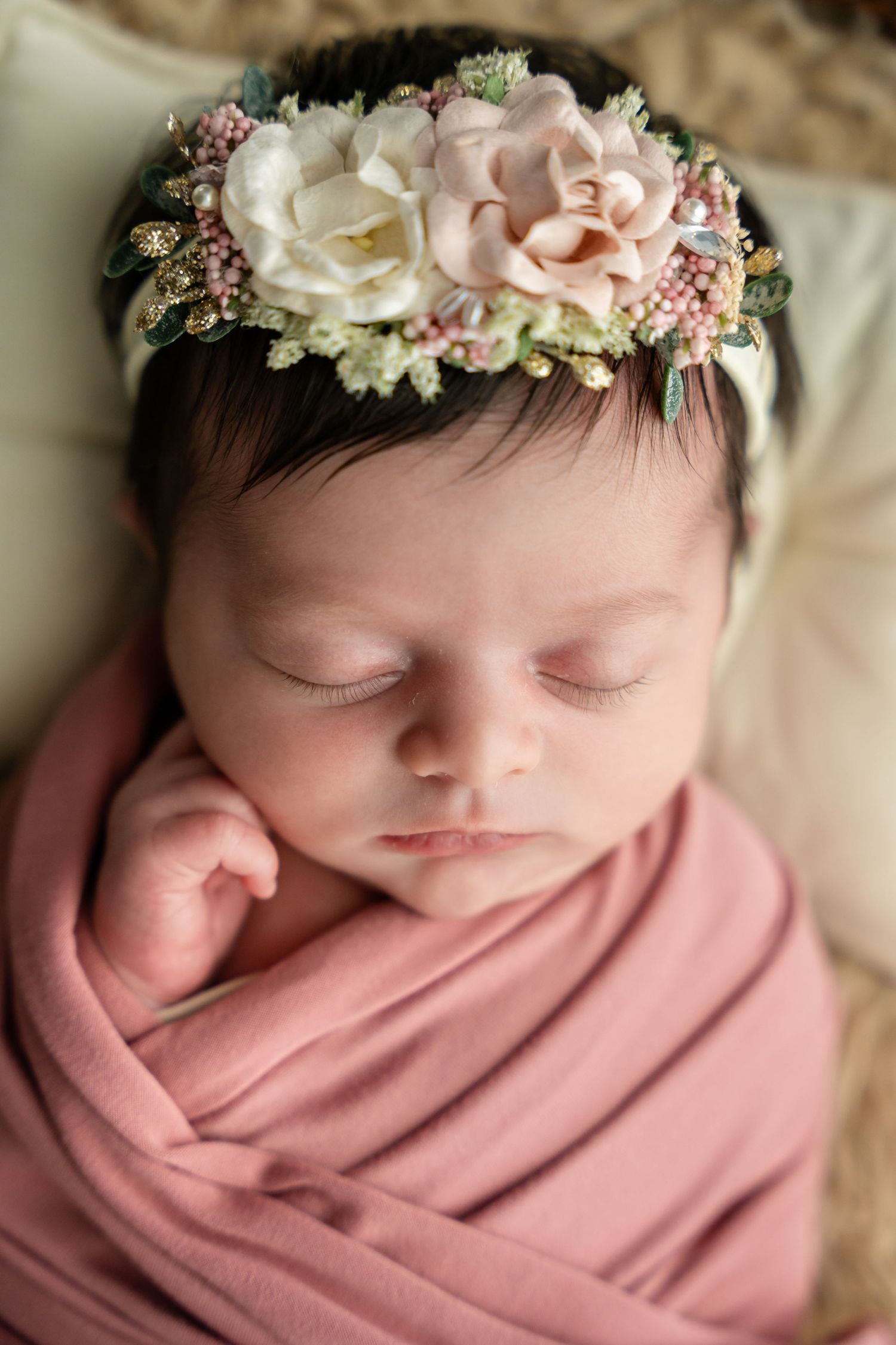 A newborn baby wearing a floral crown and wrapped in pink fabric, shown in multiple close-up shots while sleeping.