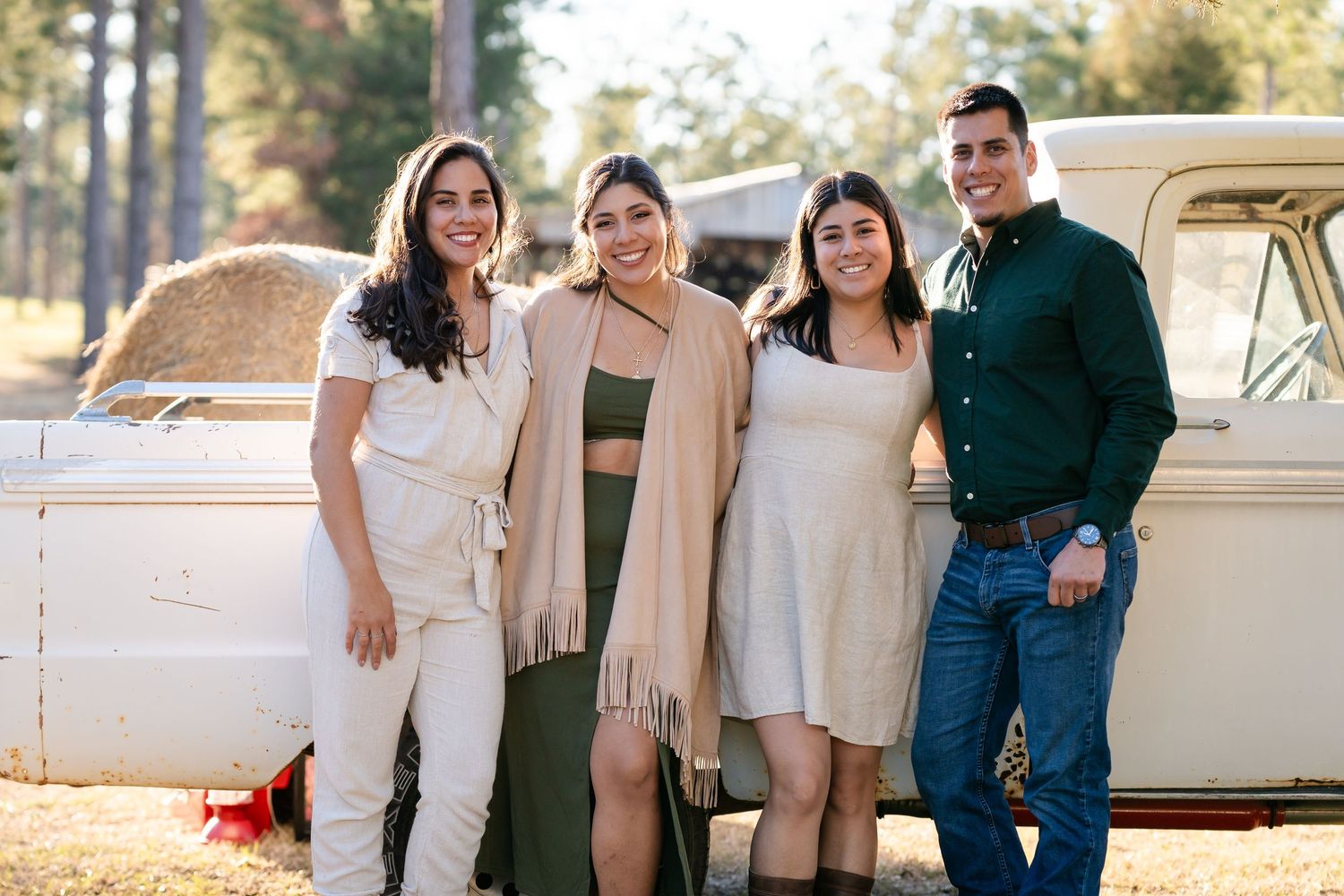 Four people pose together in coordinated outfits next to a vintage truck in a rustic outdoor setting.