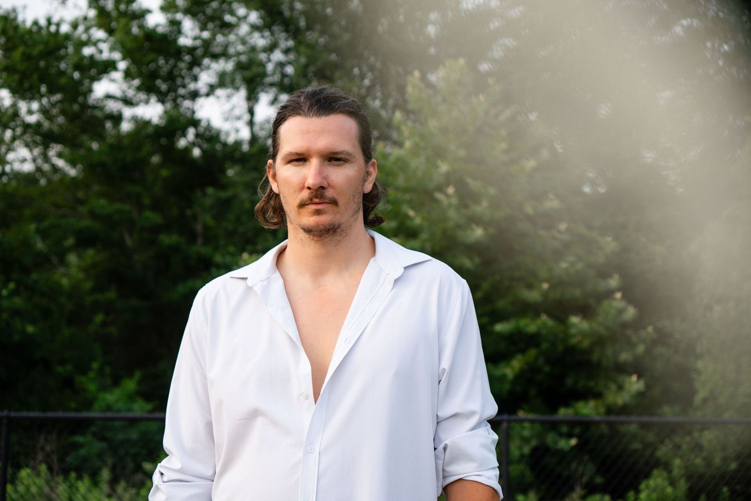 Portrait of person in white button-down shirt with sunlight streaming through trees.