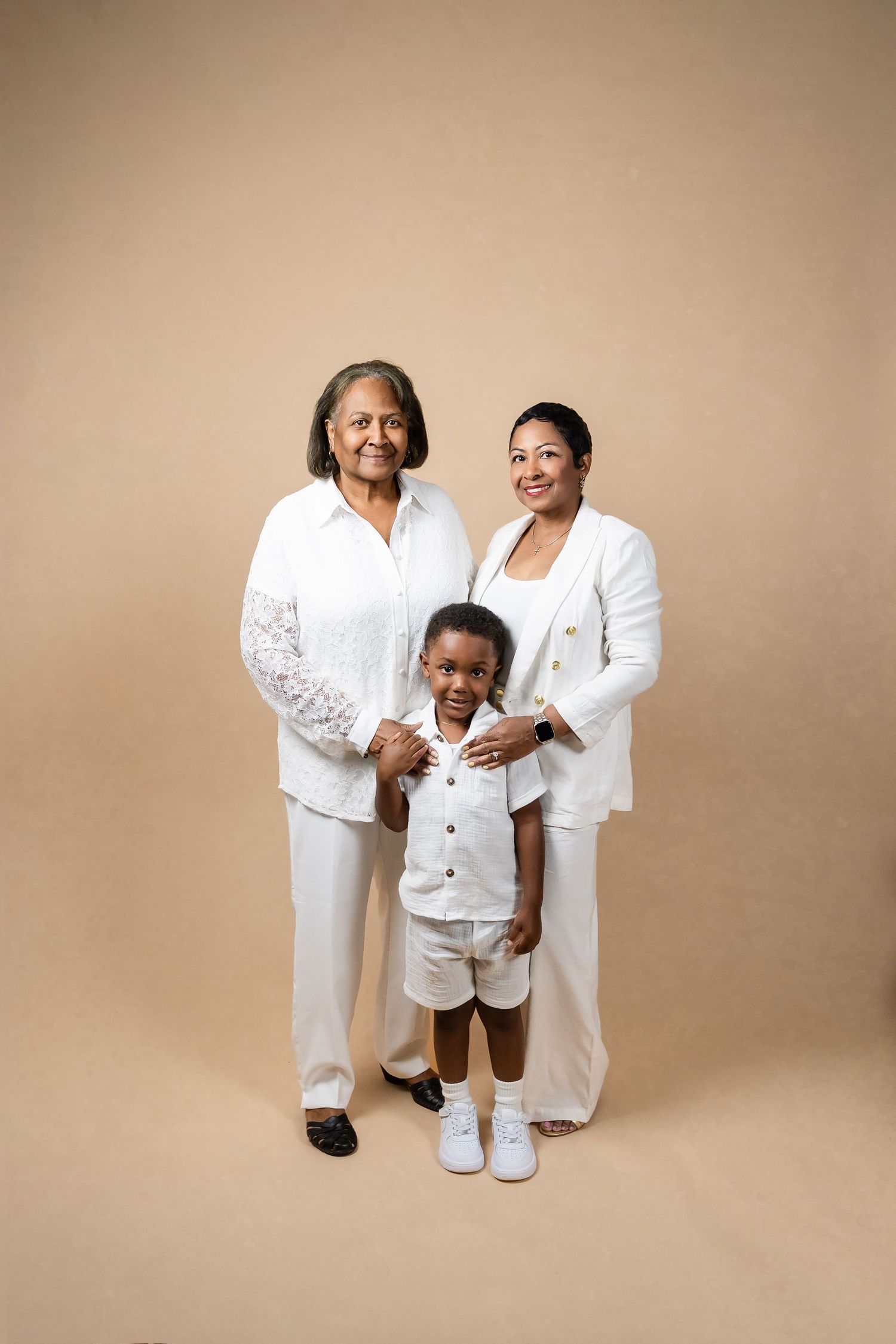 Studio portrait session of a family wearing coordinated white outfits against beige backdrop.
