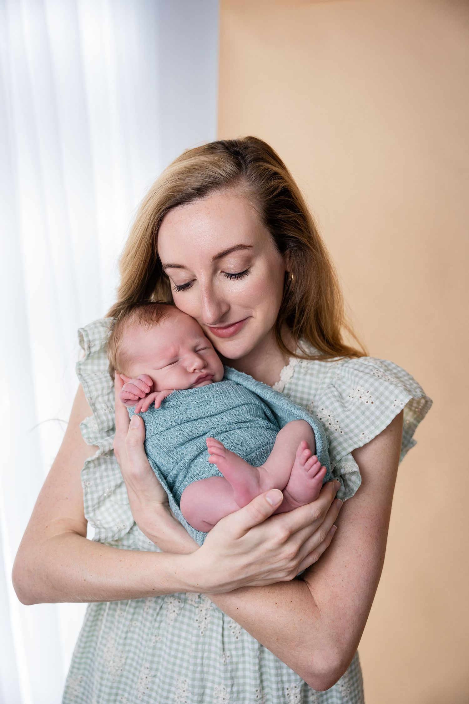 Mother in white dress holding and cuddling sleeping newborn in blue outfit.