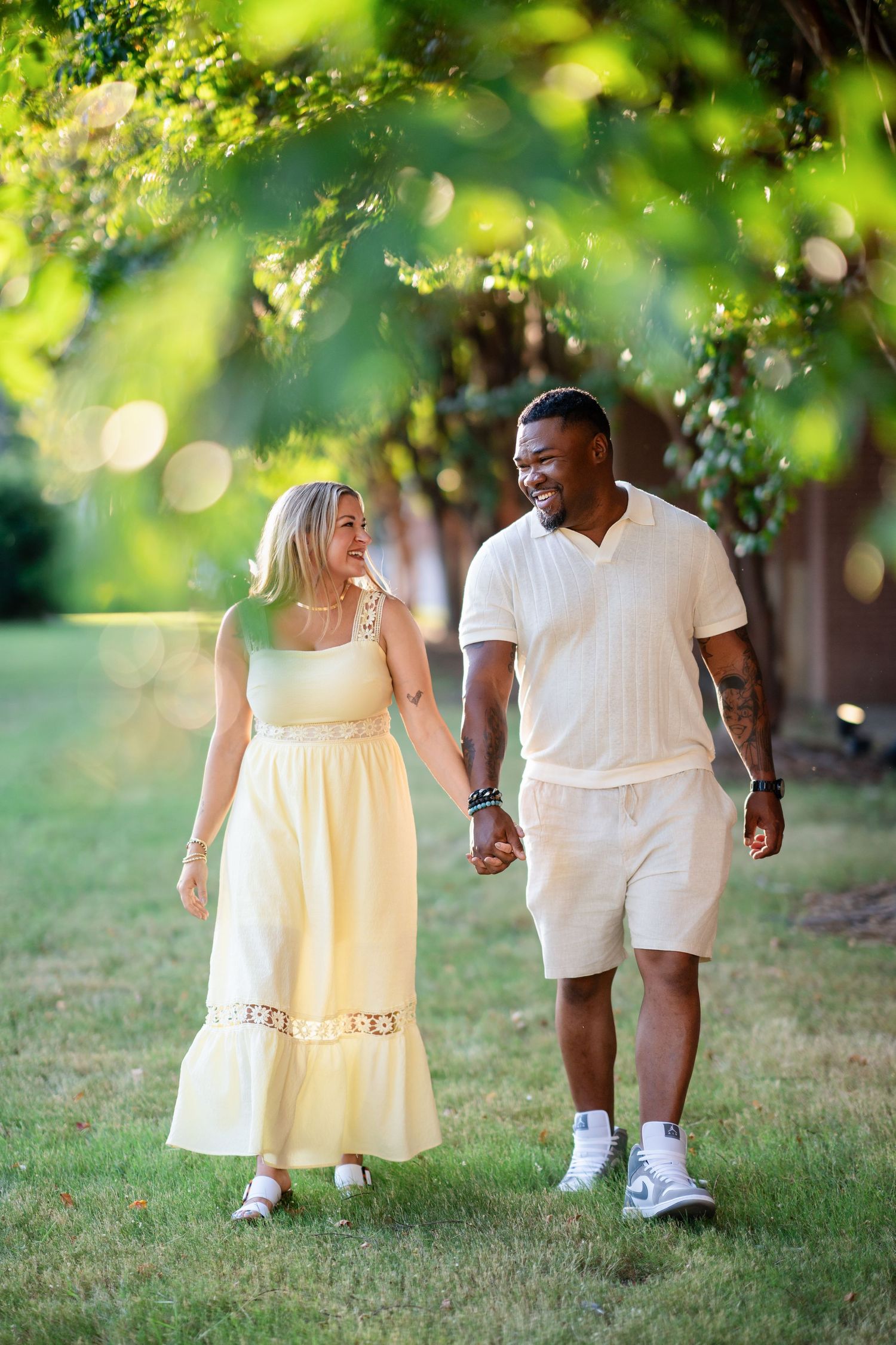 Happy interracial couple holding hands and smiling while walking together in a sunny green park.
