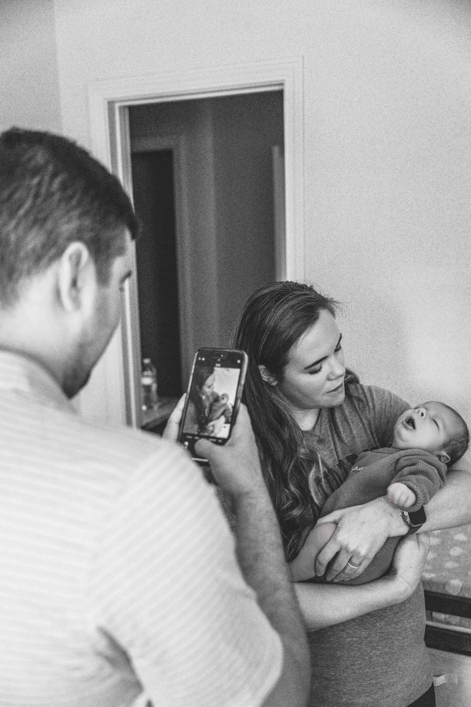 Black and white candid photo of family taking pictures with phone in living room.