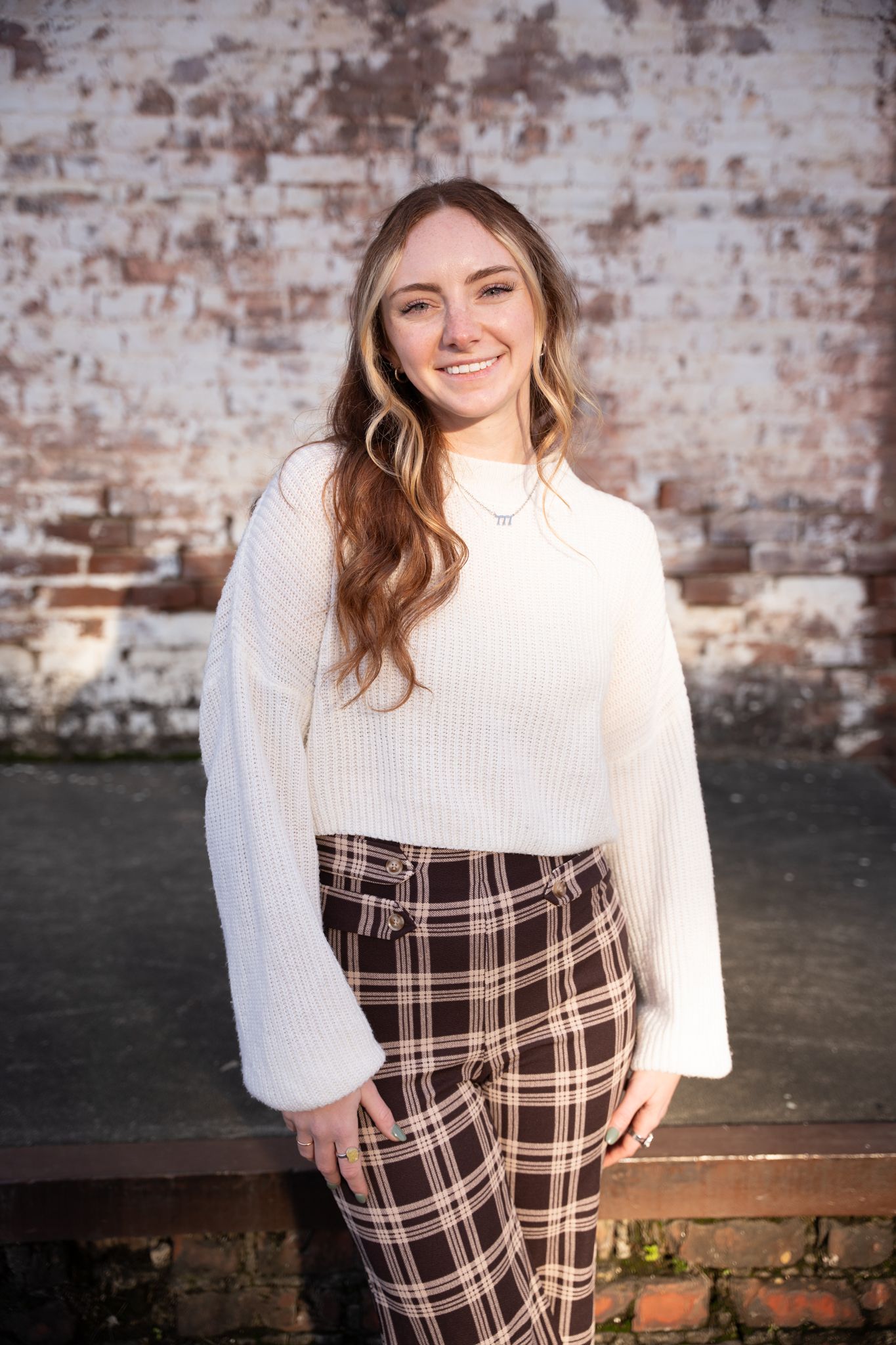 Fashion portrait against rustic brick wall showcasing cozy winter outfit with plaid pants.