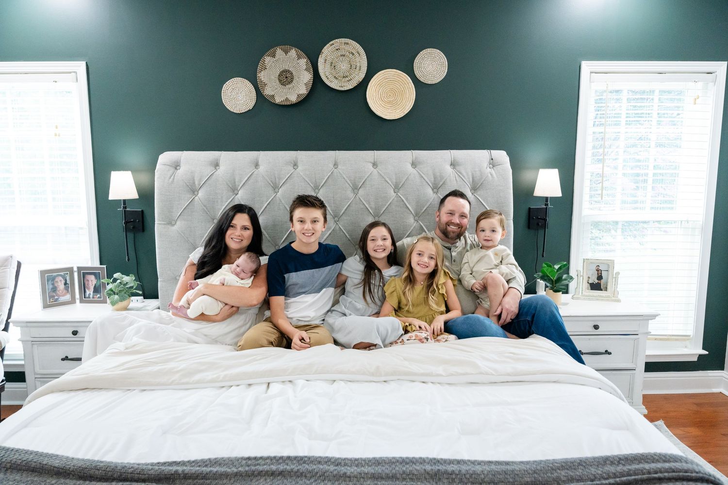 Contemporary family photo session on bed with teal accent wall and decorative elements.