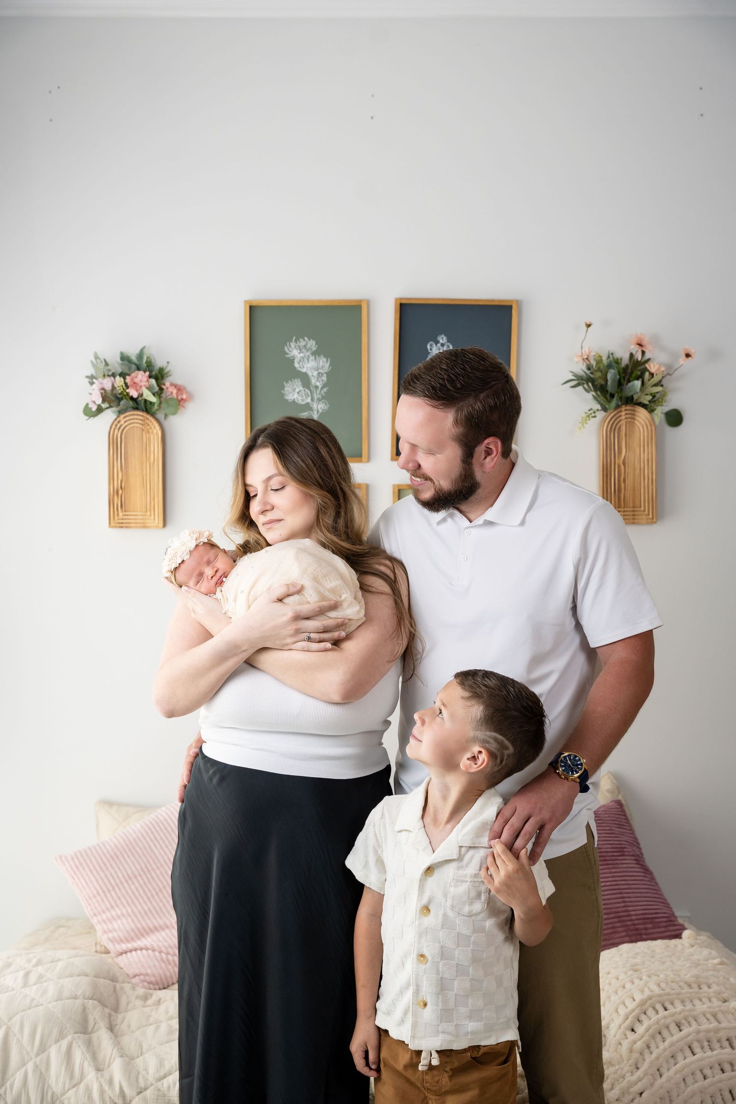 Family portrait featuring parents with their children in a bright minimalist setting with floral wall decor.