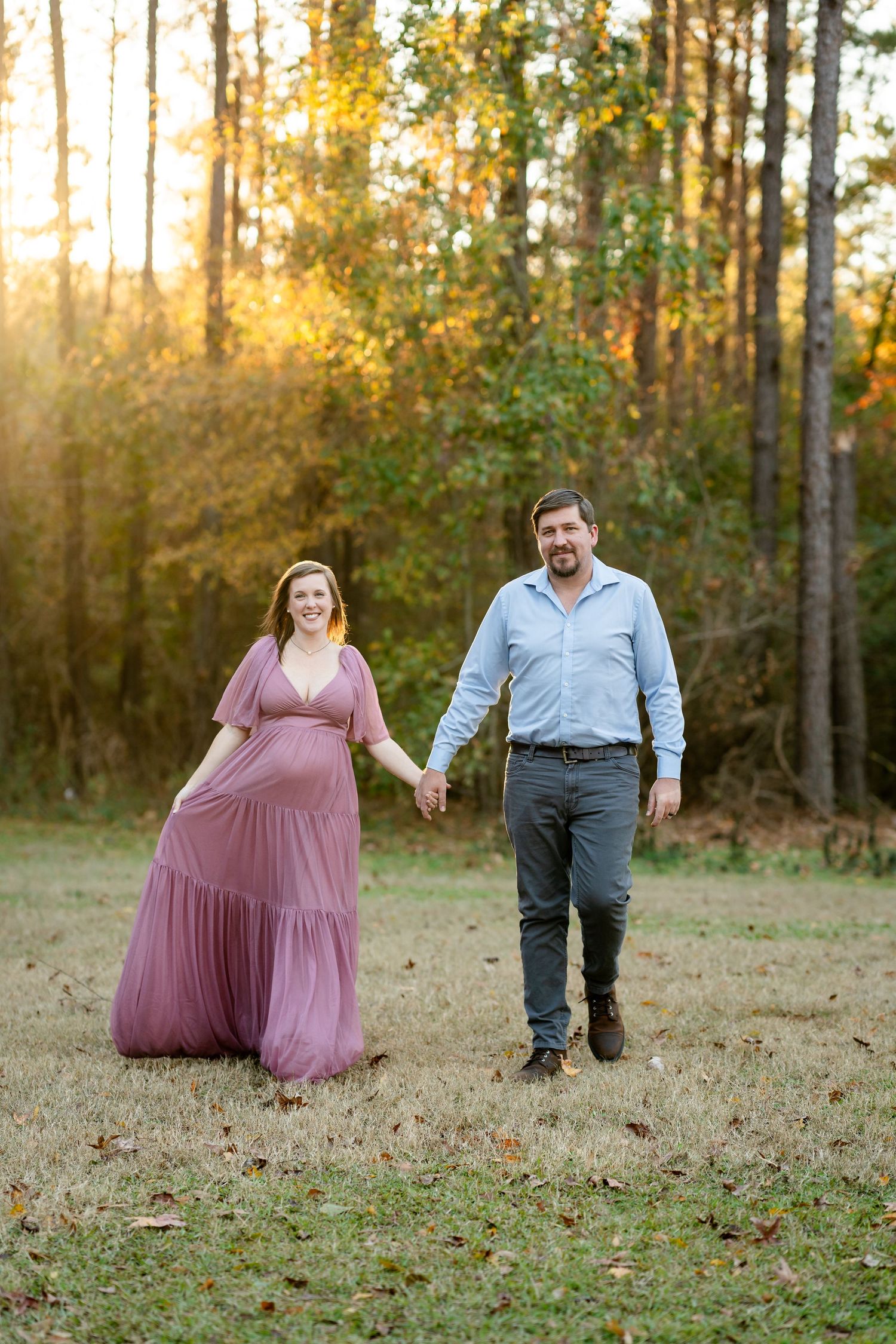 A couple dances playfully in a wooded area during golden hour.