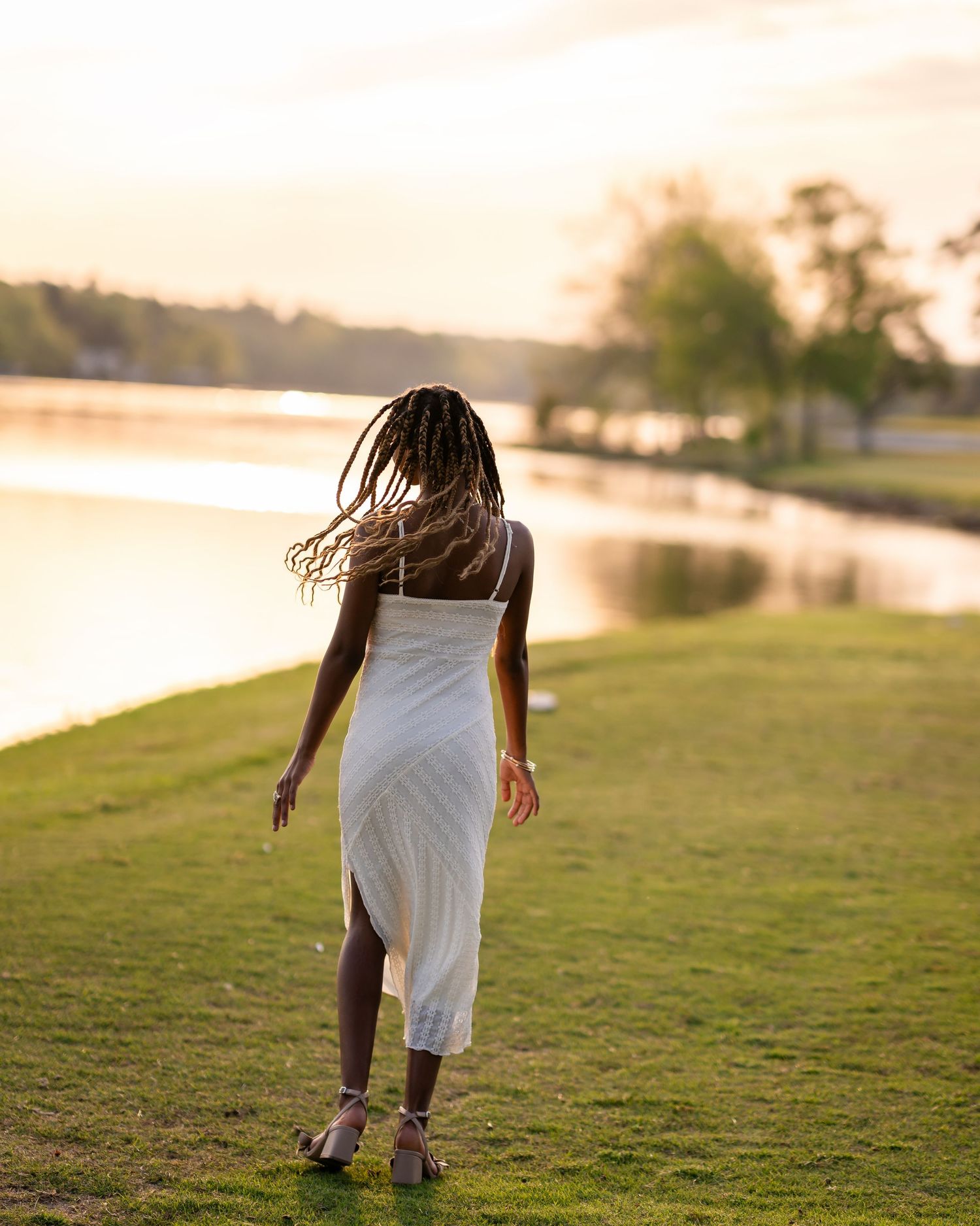 Person in white dress walking on grassy hill during golden hour.