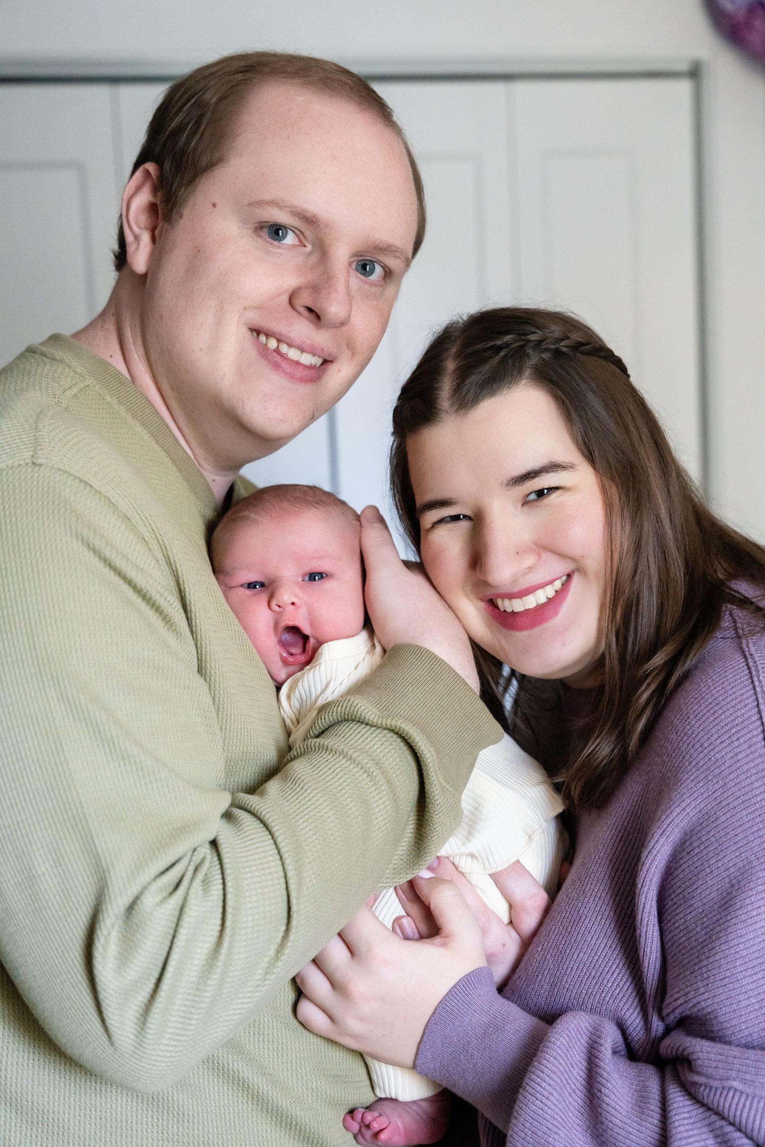 Happy couple smiling and holding their newborn baby, posing for a family portrait at home.