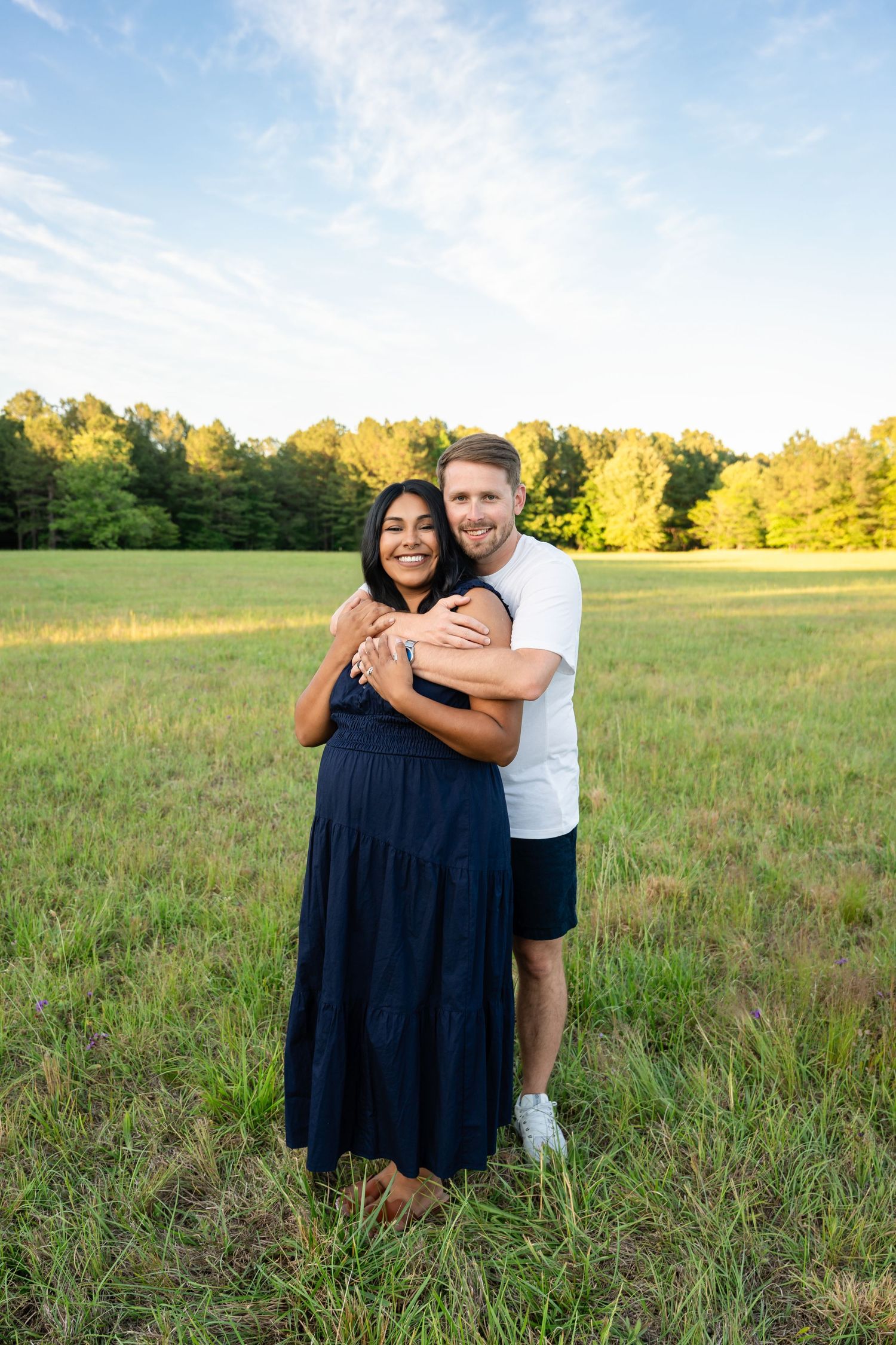 Loving couple embracing in a sunlit green meadow with trees in the background.
