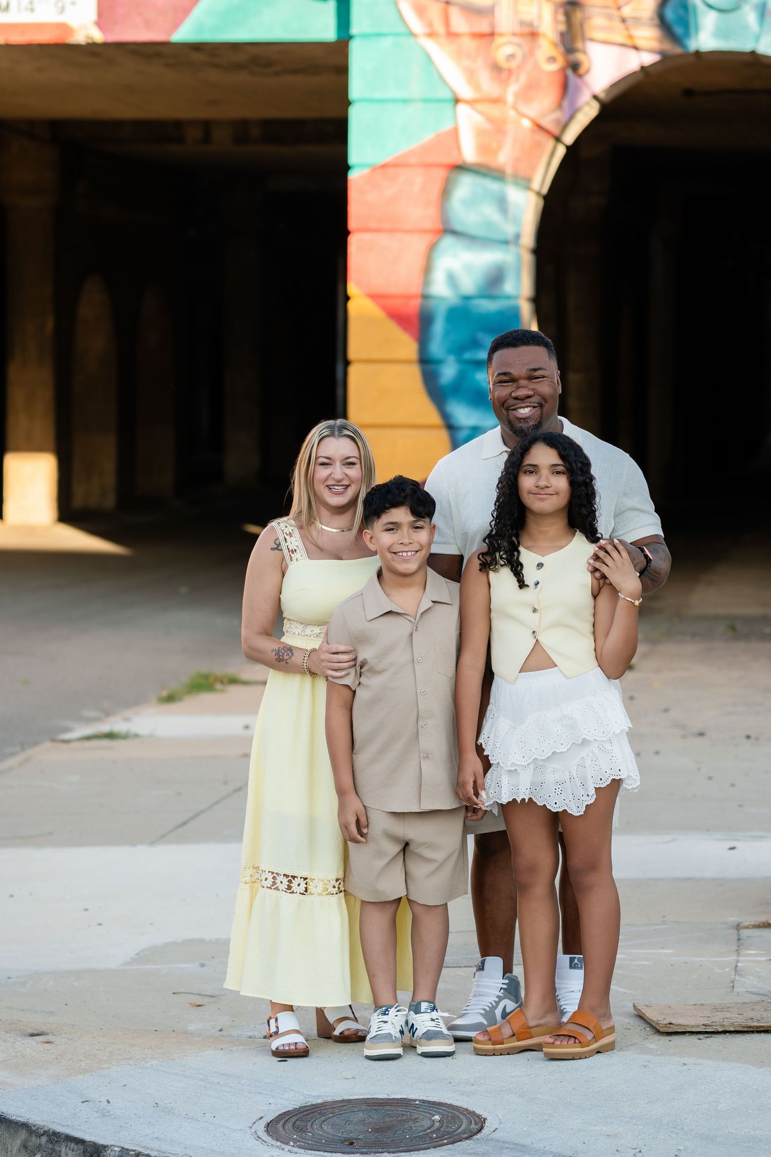 Smiling multiracial family of four poses together in front of colorful mural wall outdoors.