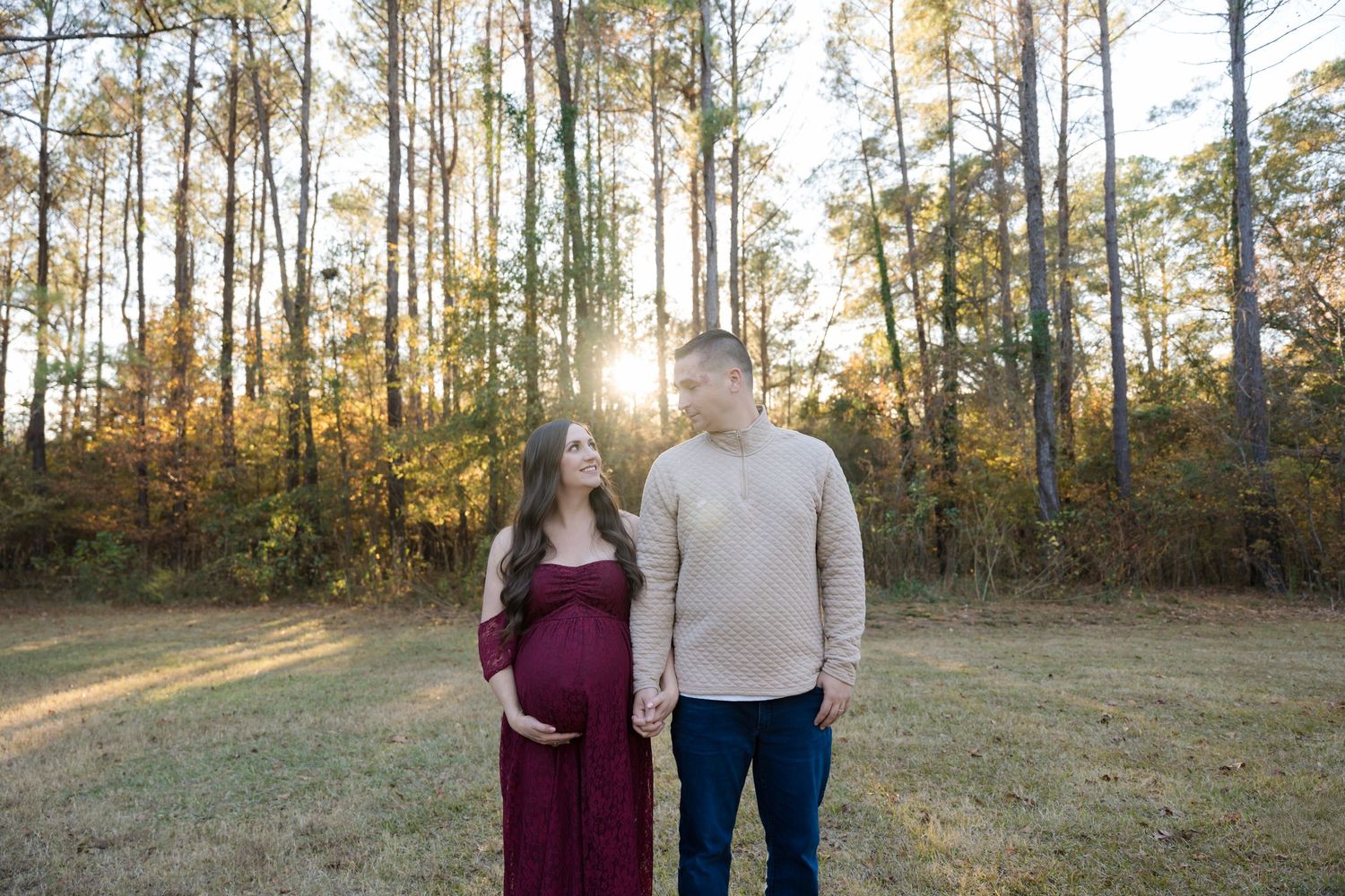 A couple stands together in a sunlit autumn forest clearing during golden hour.