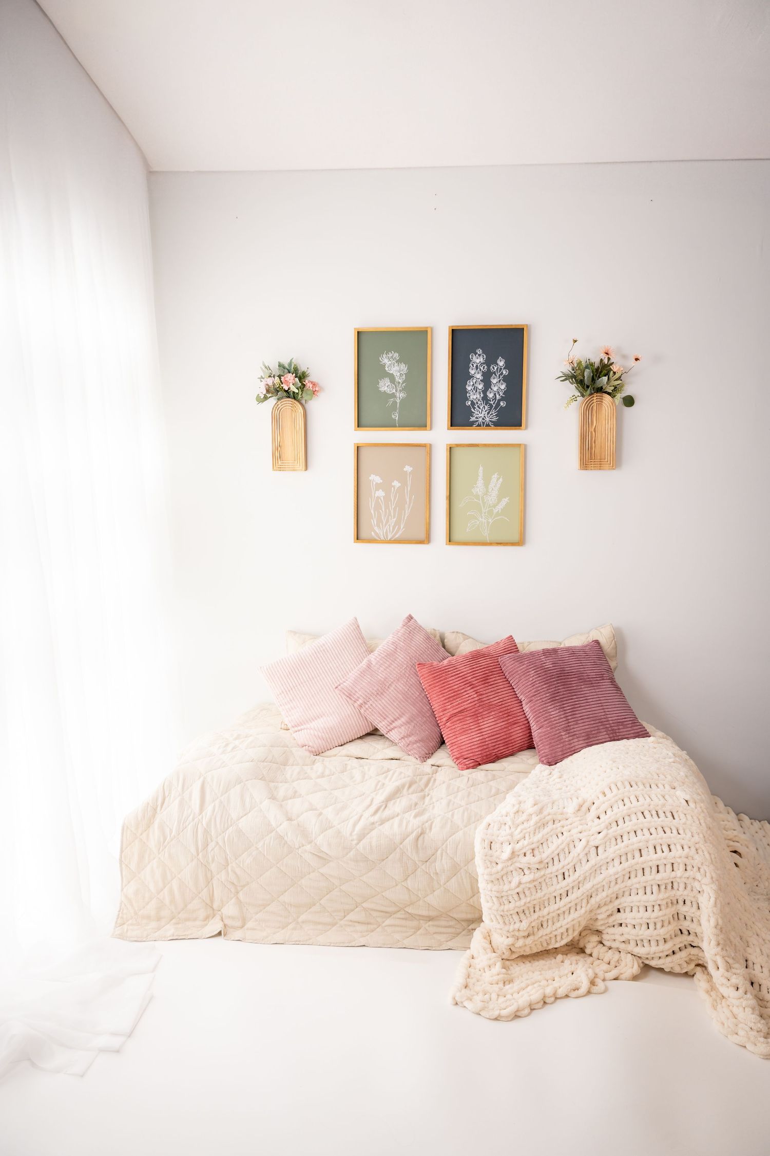 Minimalist bedroom setup with cream bedding and pink pillows against white wall with framed art.