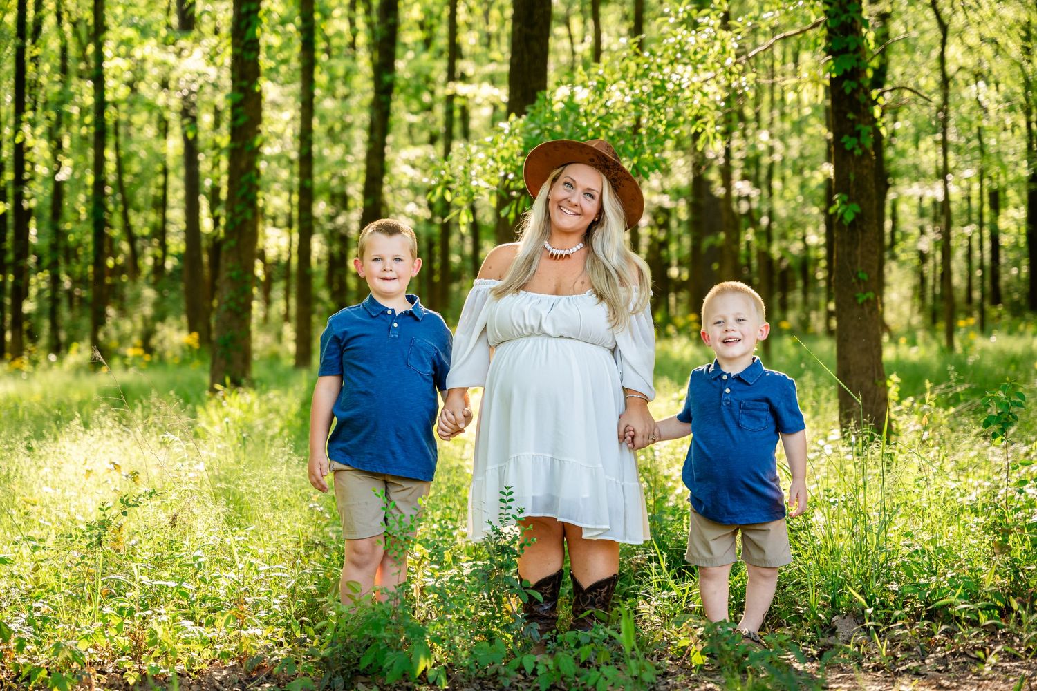 Family portrait session in a sunlit forest with tall trees and green undergrowth.