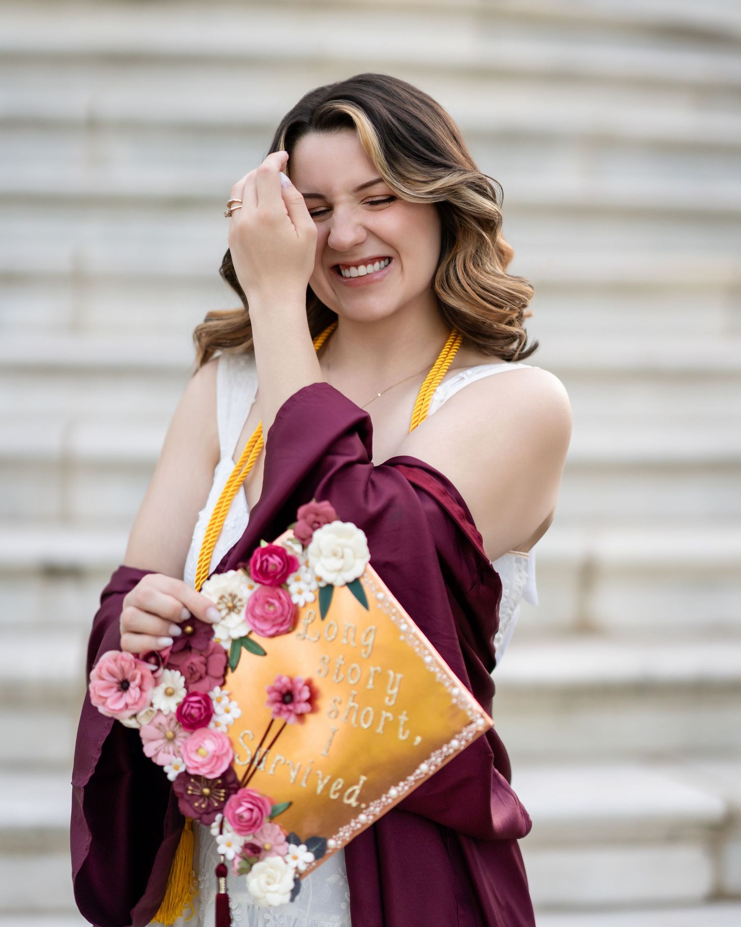 Graduate holding decorated books with pink flowers against white stone columns.