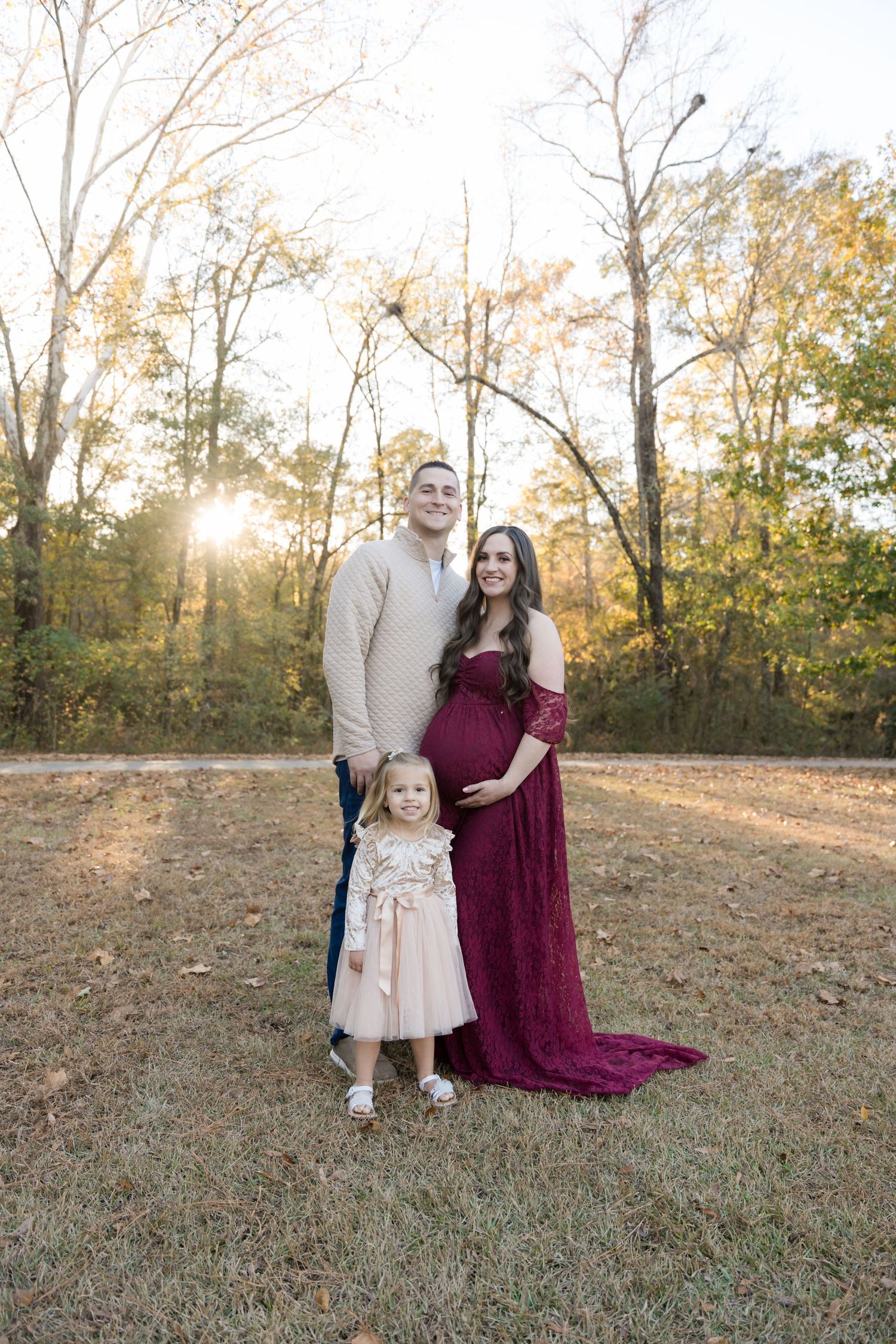 A family poses together outdoors in autumn, wearing formal attire against a backdrop of sunlit trees.