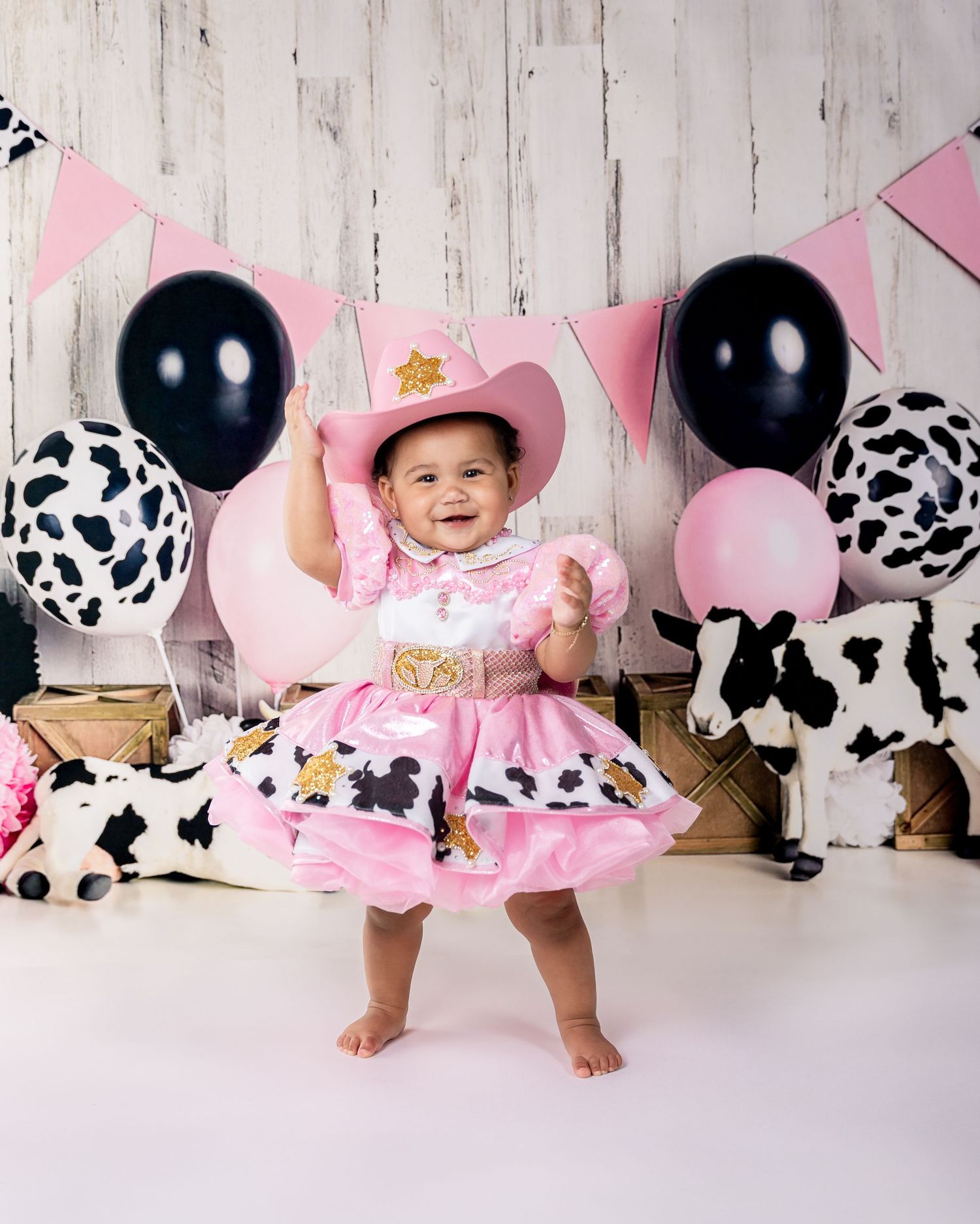 Pink and black cow print themed backdrop with balloons and bunting decorations.