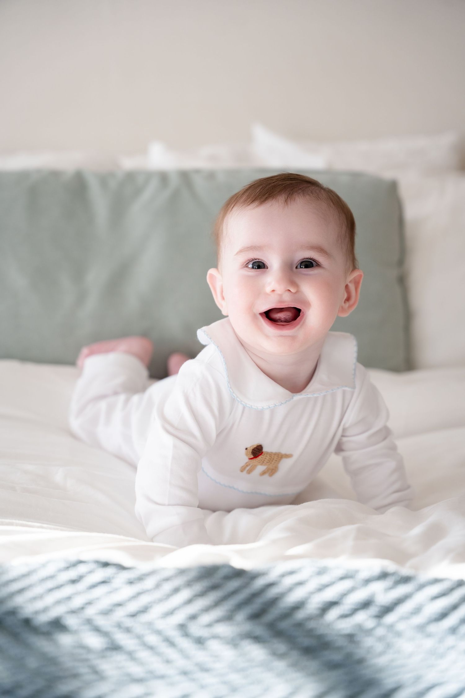 Baby in white onesie smiling brightly during indoor photo session.
