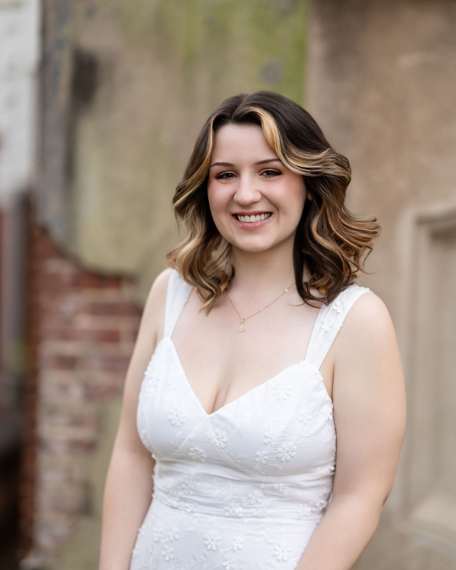 Person in elegant white dress poses against rustic brick and stone architectural backdrop.