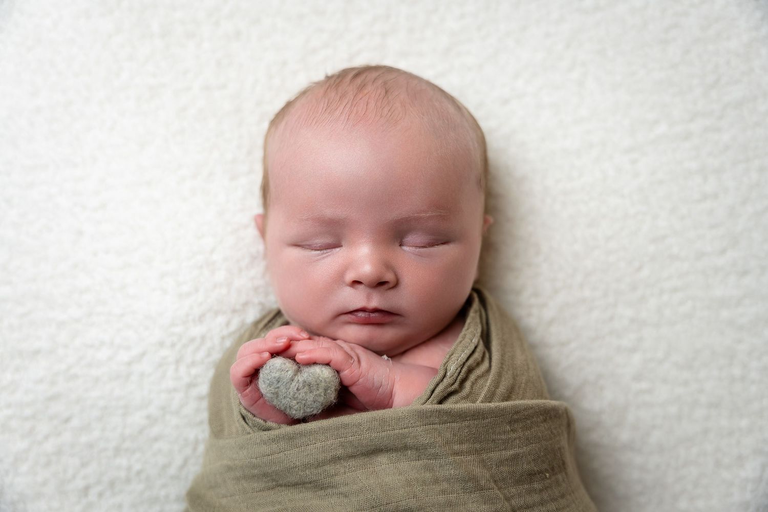 Peaceful sleeping newborn with hands tucked under chin wrapped in tan fabric.