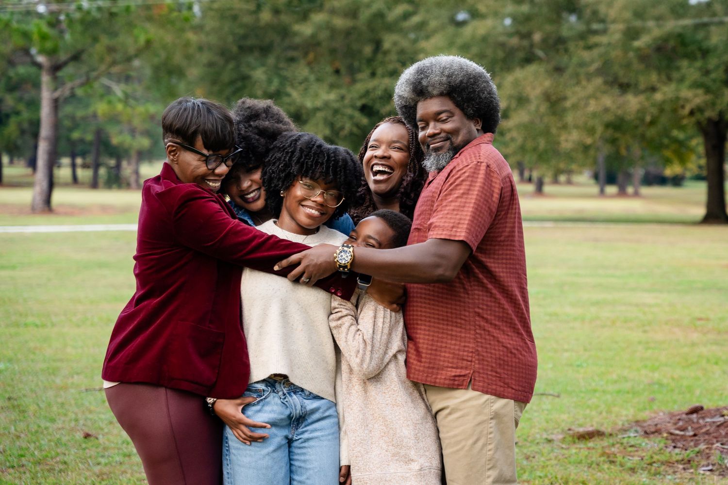 Friends sharing laughs and hugs during an outdoor photoshoot in a park setting.