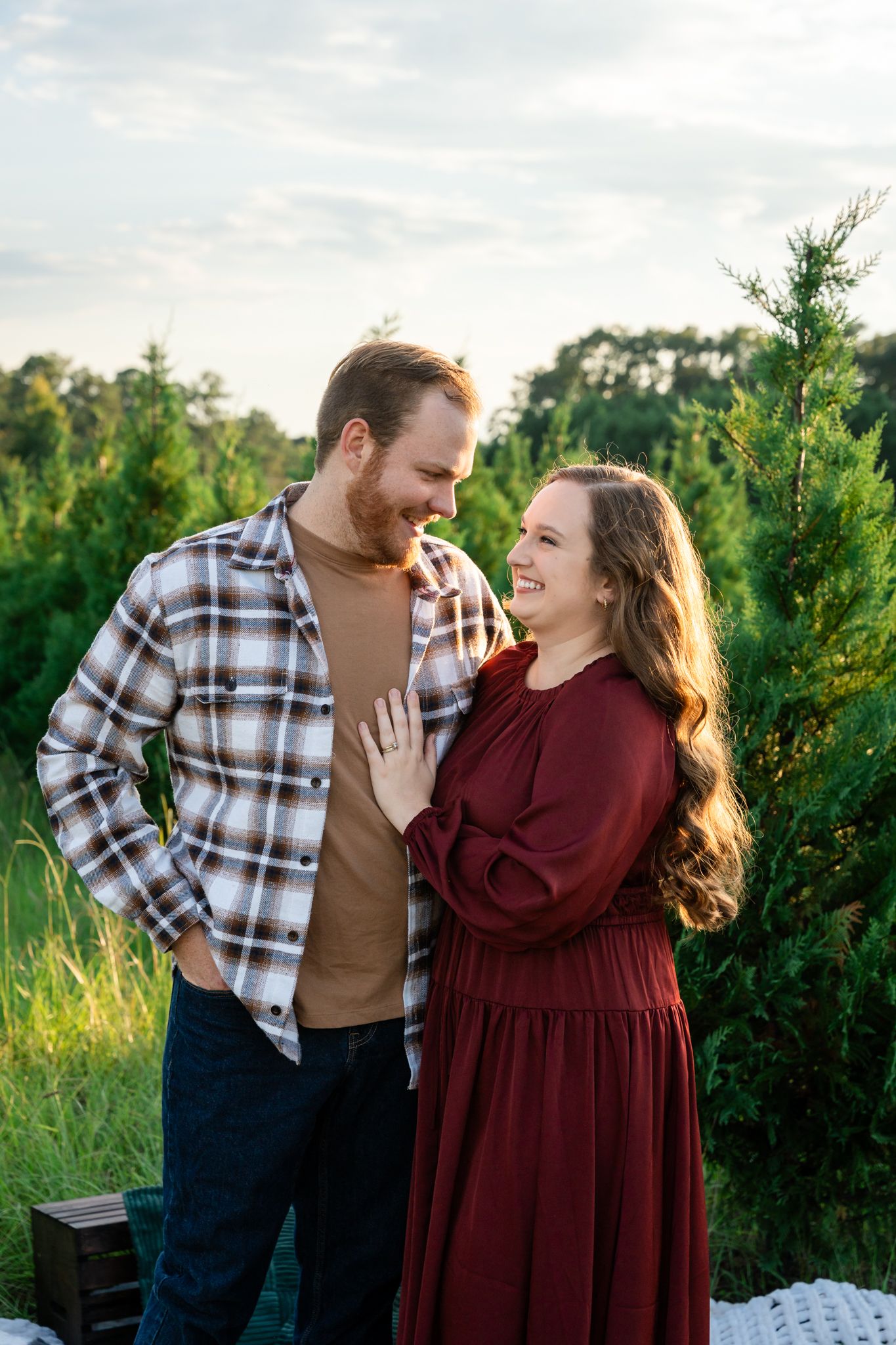 Couple sharing joyful moments outdoors near evergreen trees at sunset.