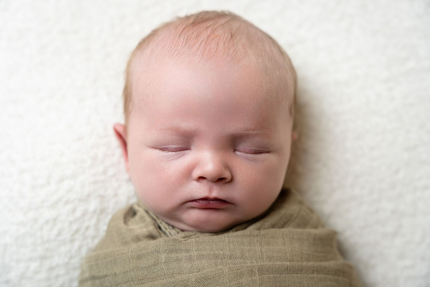 Peaceful sleeping newborn wrapped in soft white swaddle.