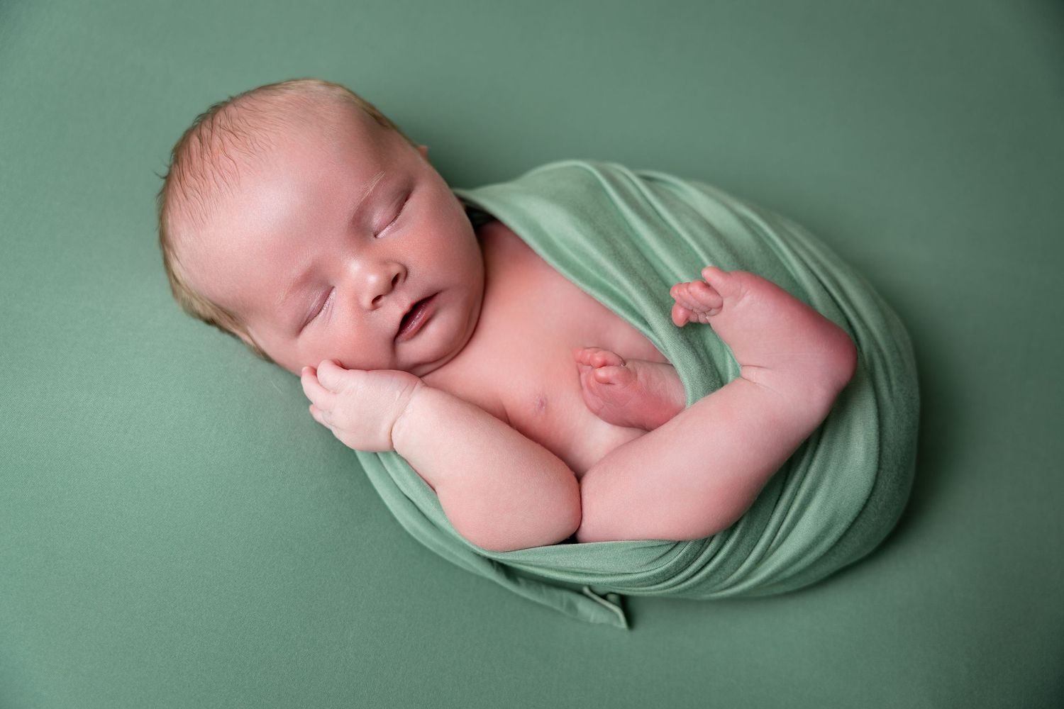 Artistic newborn photography poses on mint green background with soft wrapping.