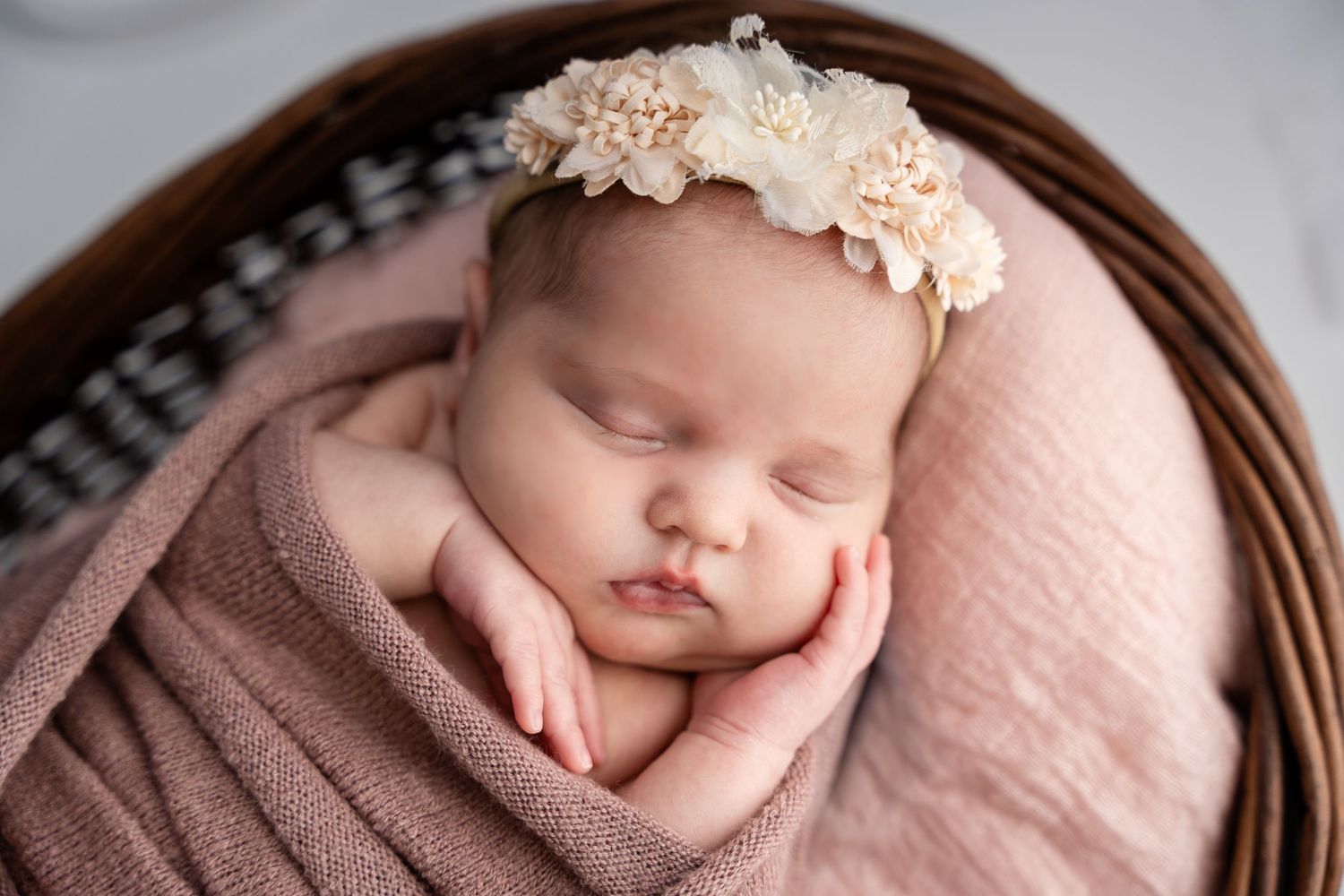 Sleeping newborn baby wrapped in pink swaddling cloth wearing a delicate floral headband.