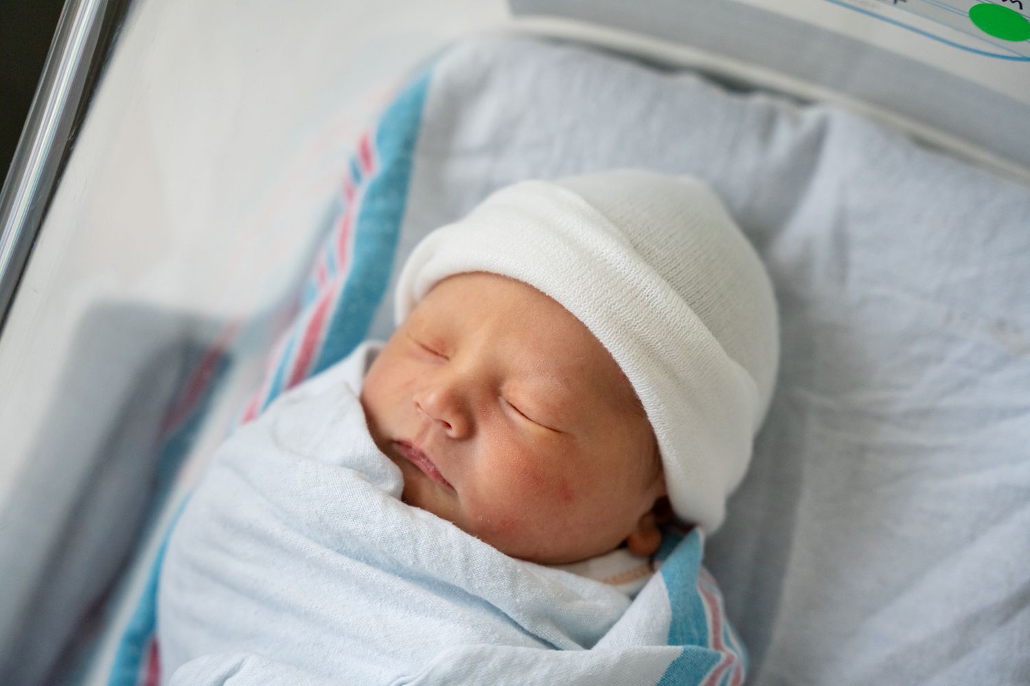 Sleeping newborn wearing white cap on blue and white bedding.