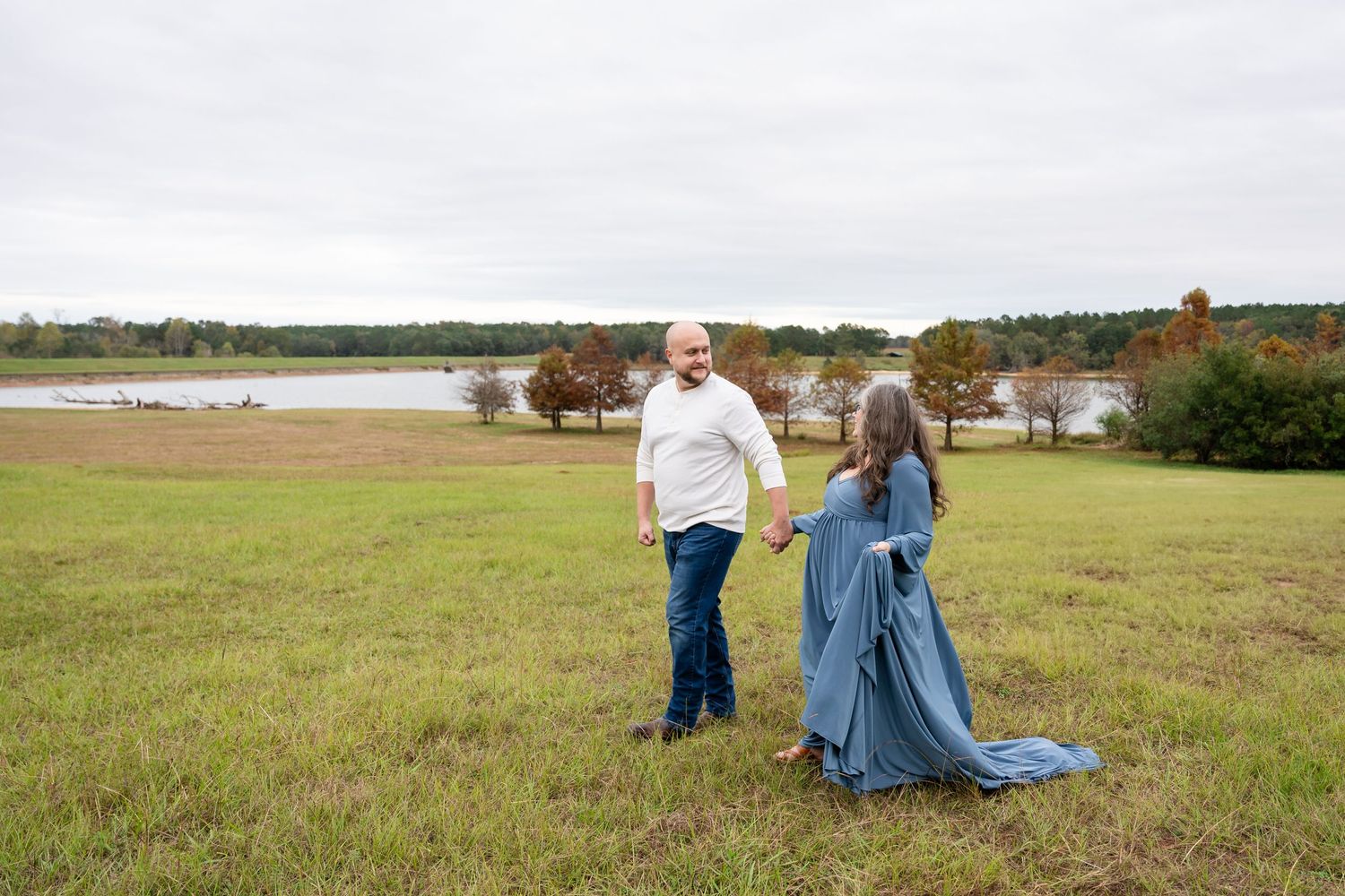 Panoramic maternity photos in open field with water and autumn trees.