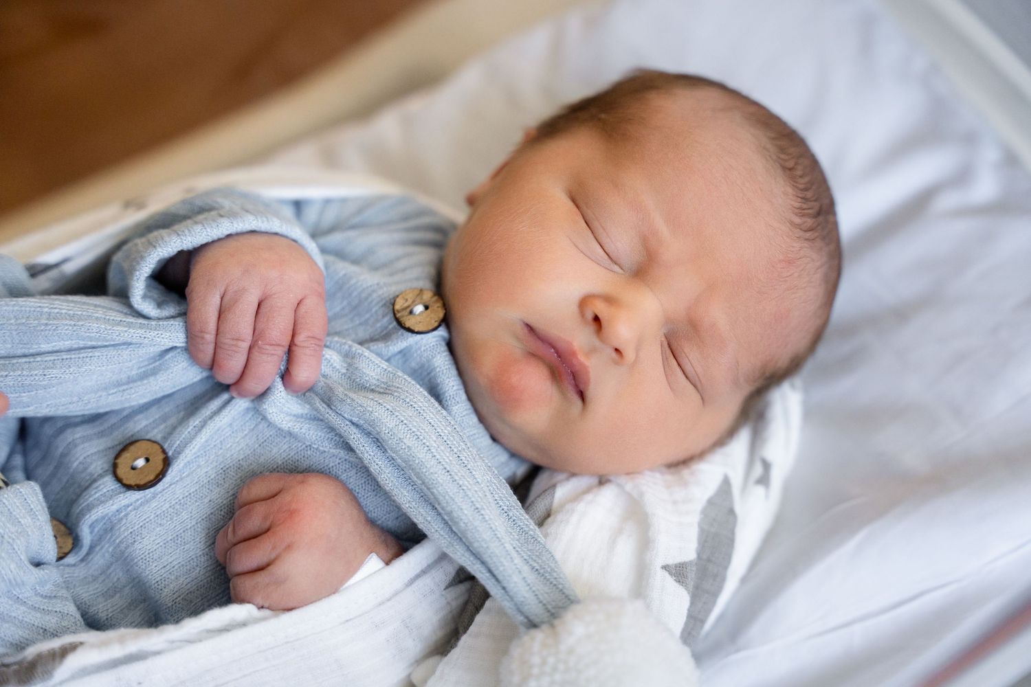 Infant resting in light blue outfit on white bedding.