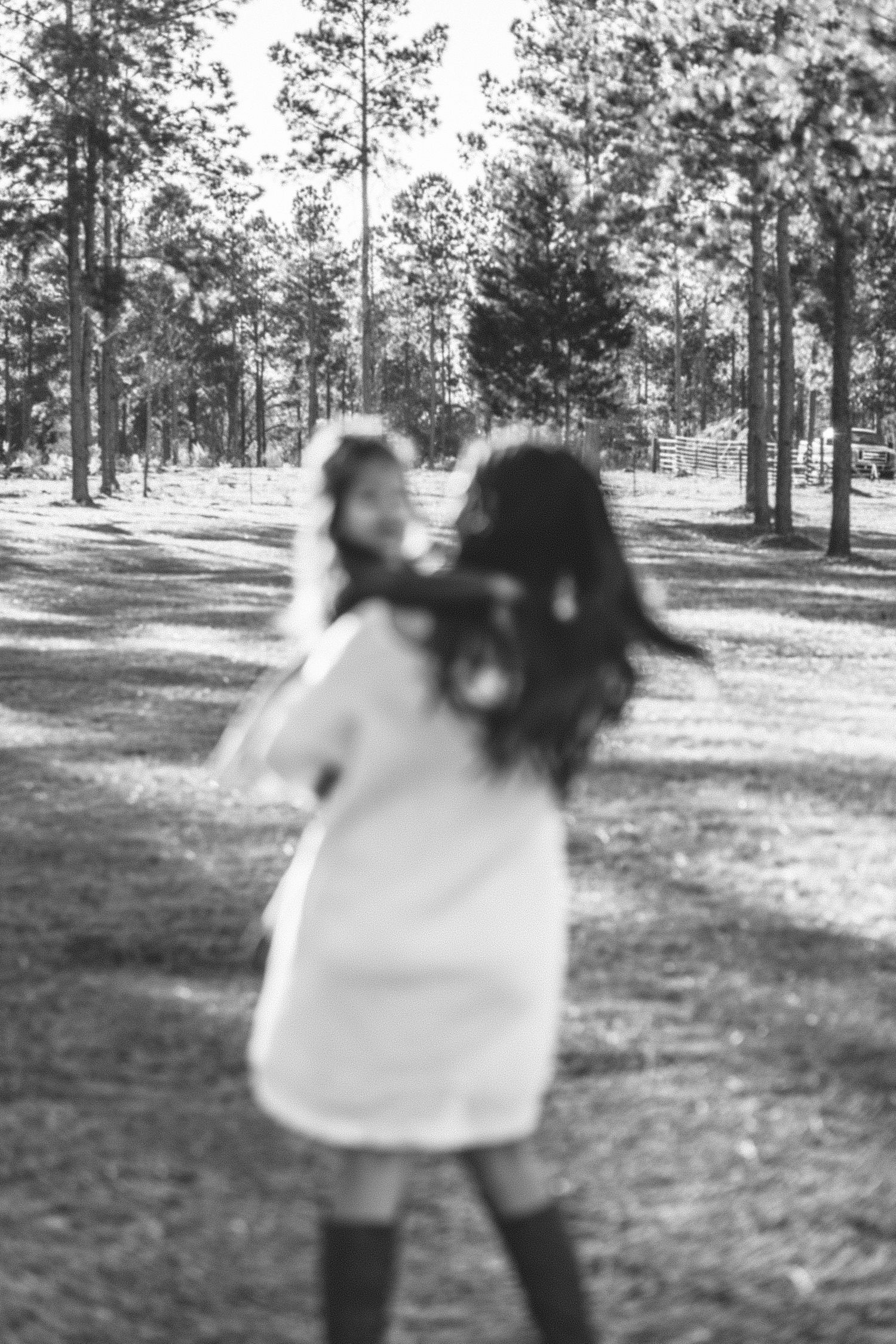 Artistic black and white photo of figures in motion outdoors among pine trees.