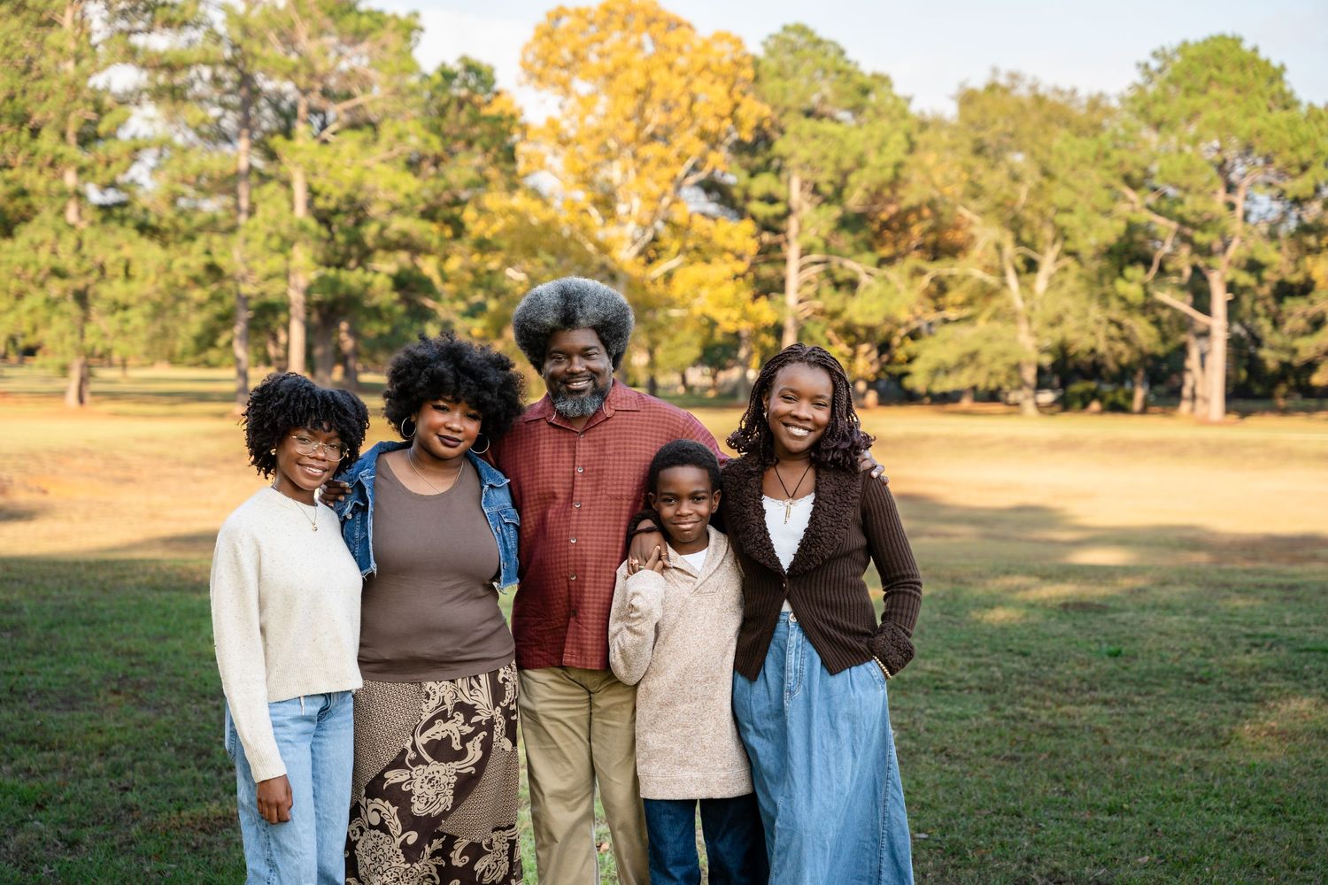 Family posing together outdoors in a grassy field during golden hour with pine trees in the background.