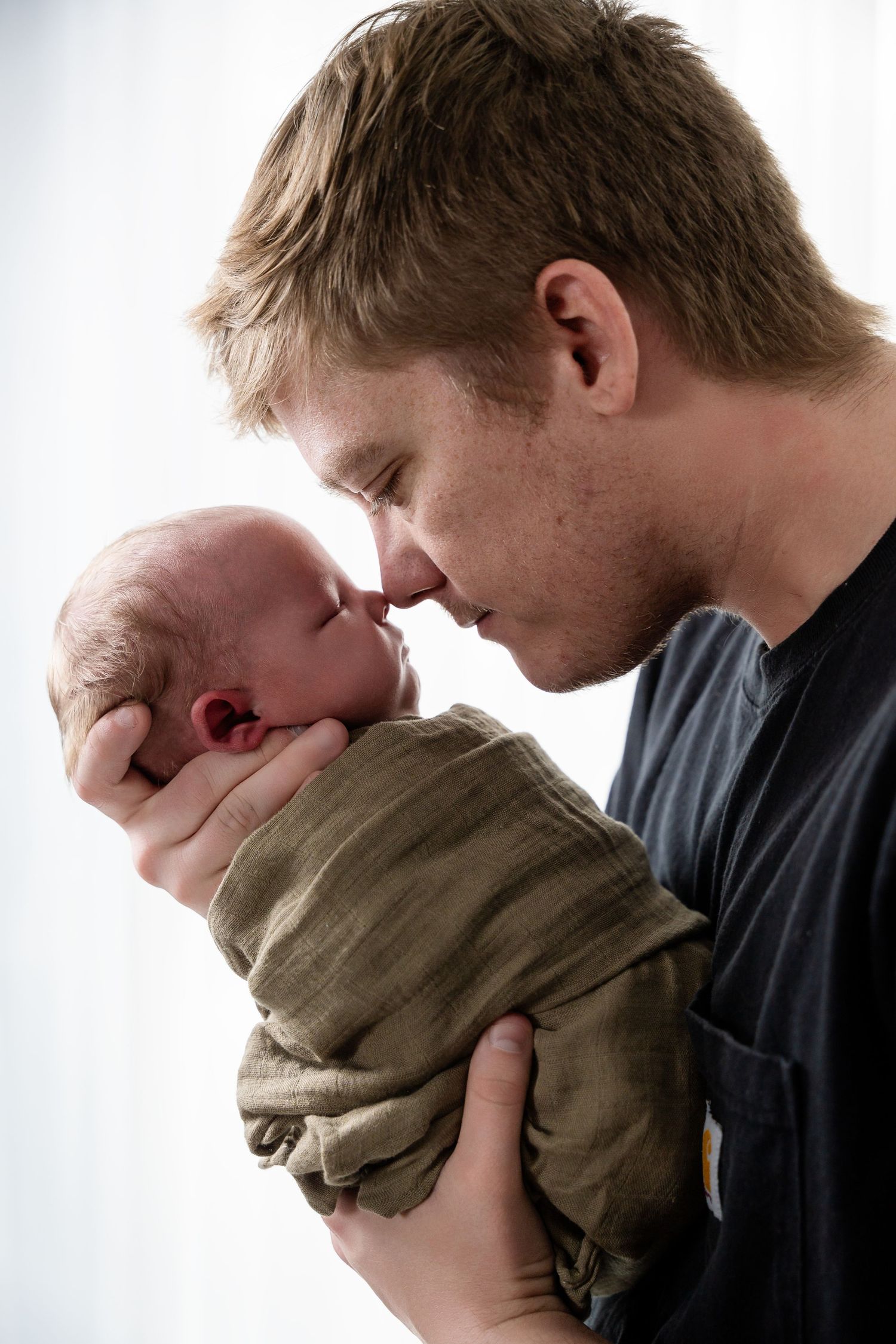 Parents embrace and kiss their swaddled newborn in a series of intimate studio portraits.