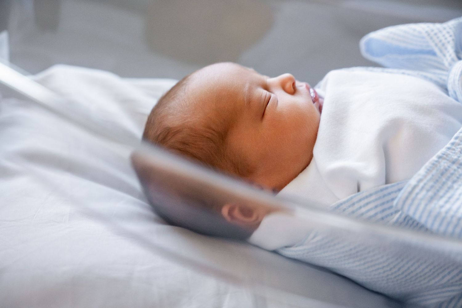 Newborn sleeping peacefully in soft white and blue bedding.