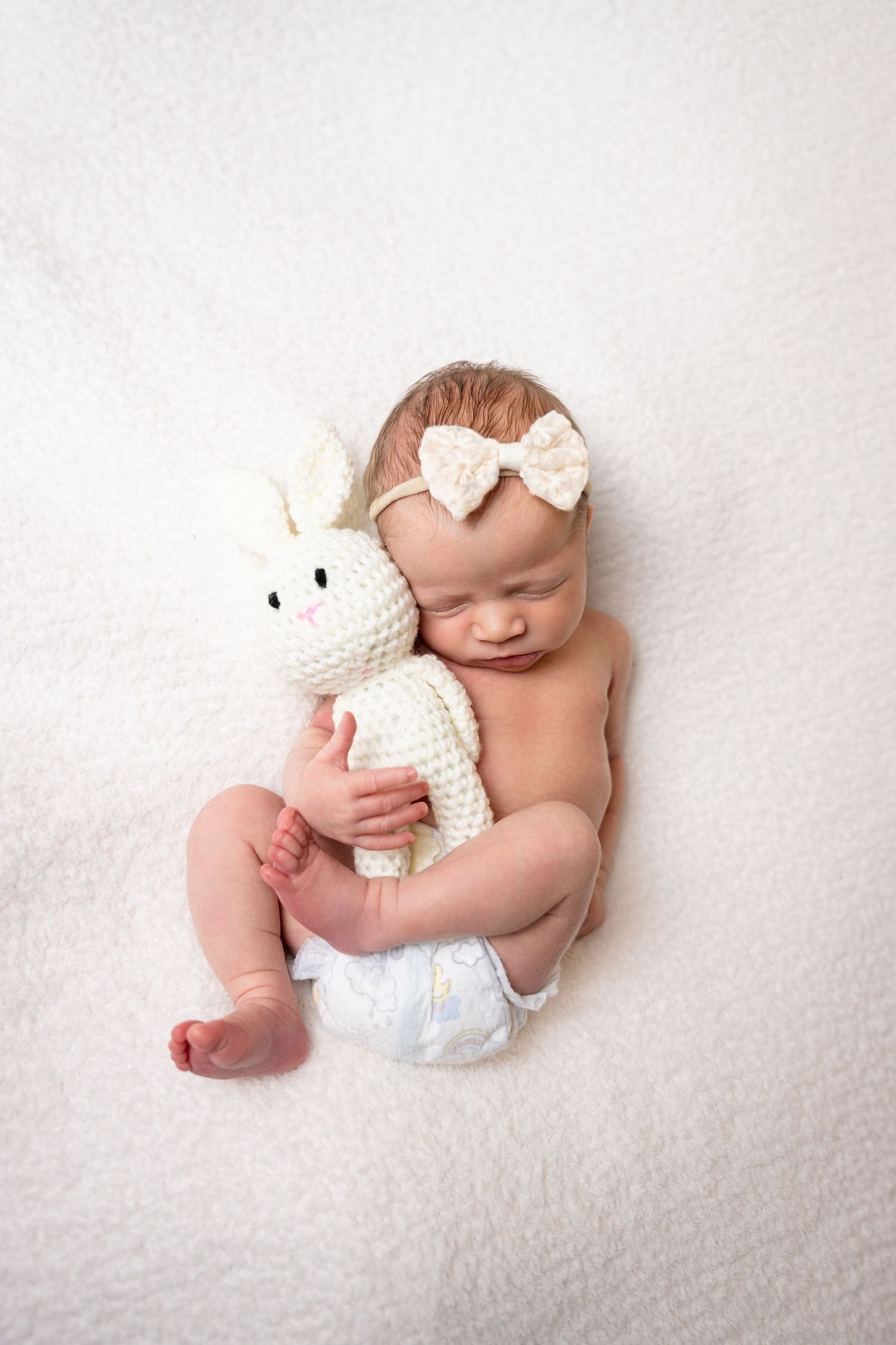 Baby cuddling white stuffed unicorn toy on white backdrop.